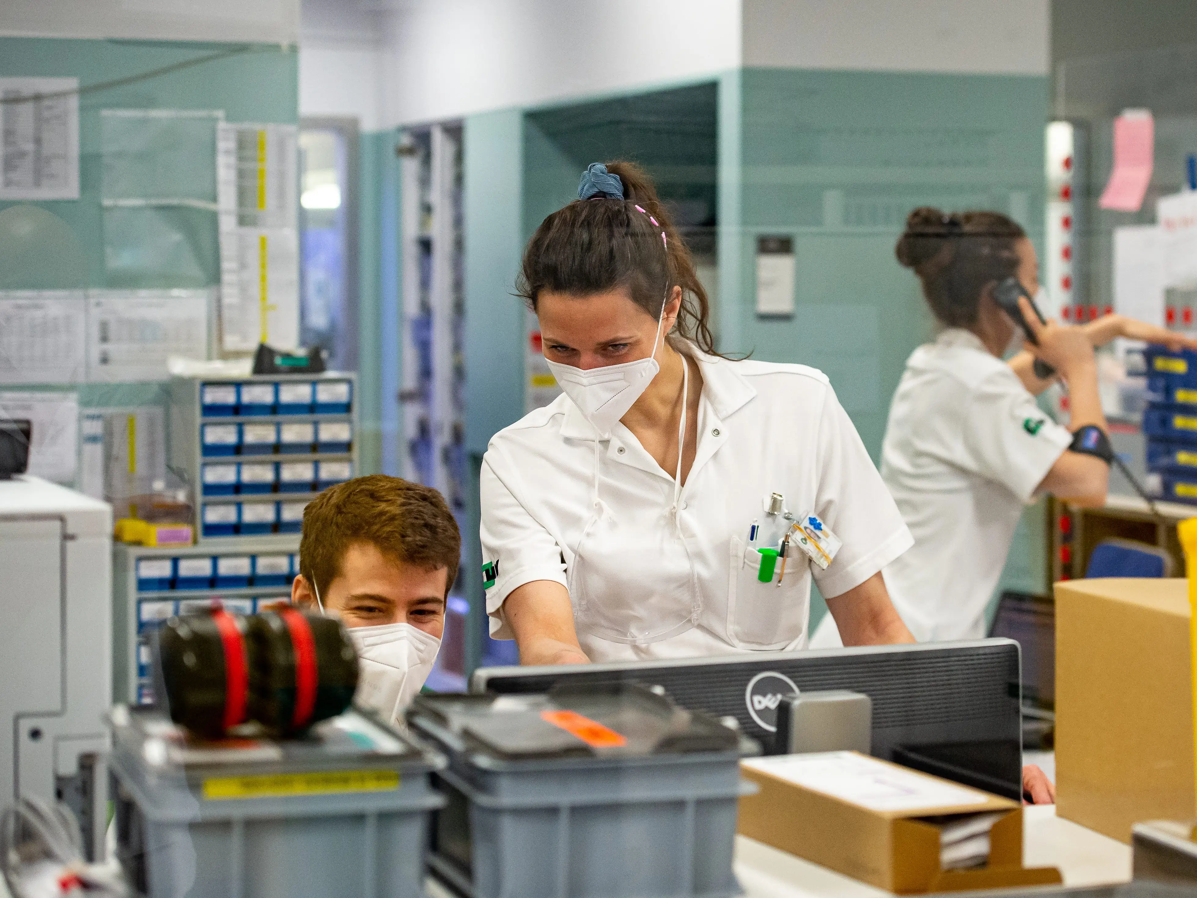 Two Swiss nurses in face masks talking to each other in front of a computer
