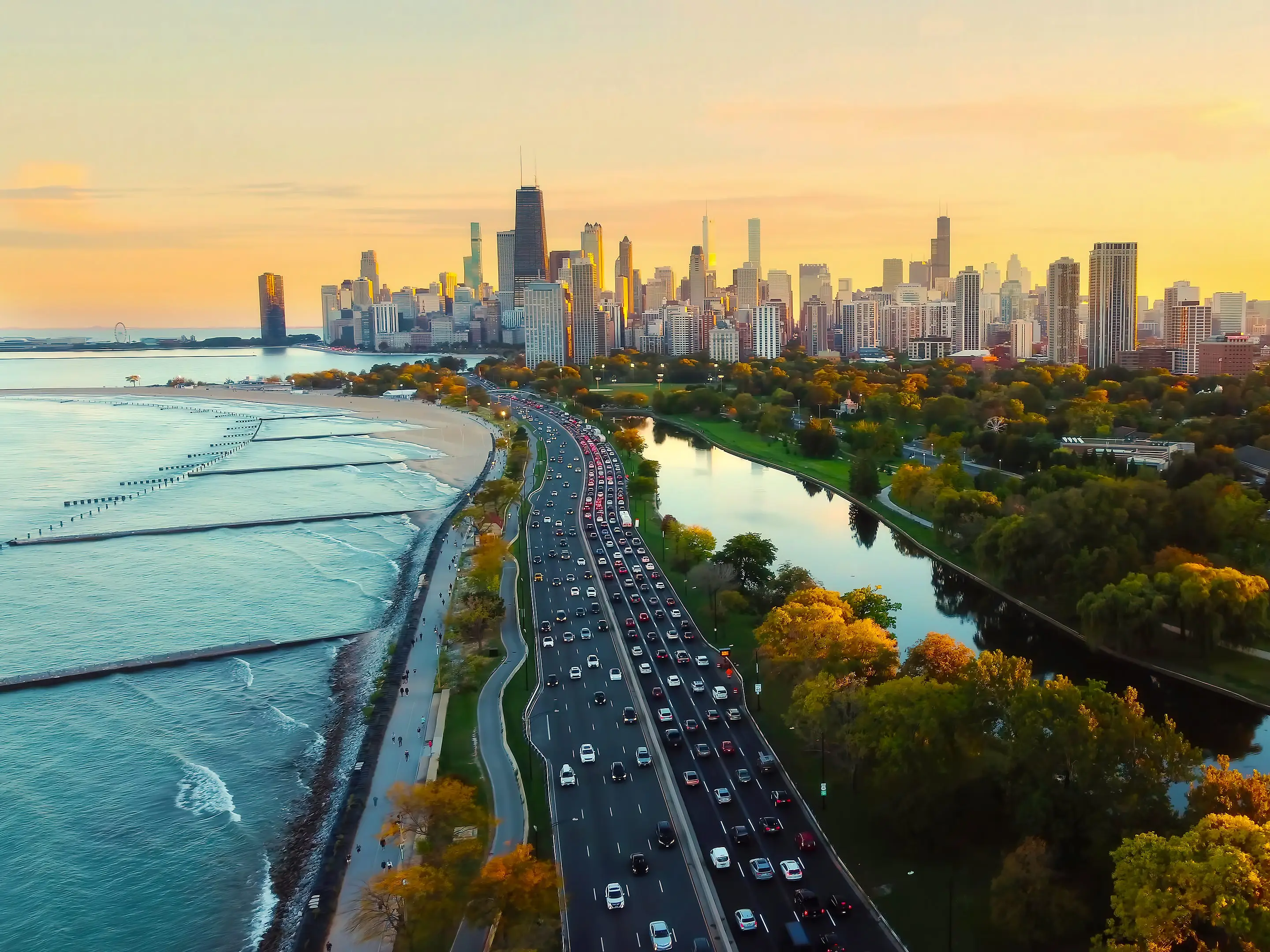 Chicago Cityscape at Sunset with Lakefront View. Aerial view of Chicago skyline at sunset, showing Lake Michigan shoreline, tree-lined parks, and a busy roadway along the waterfront