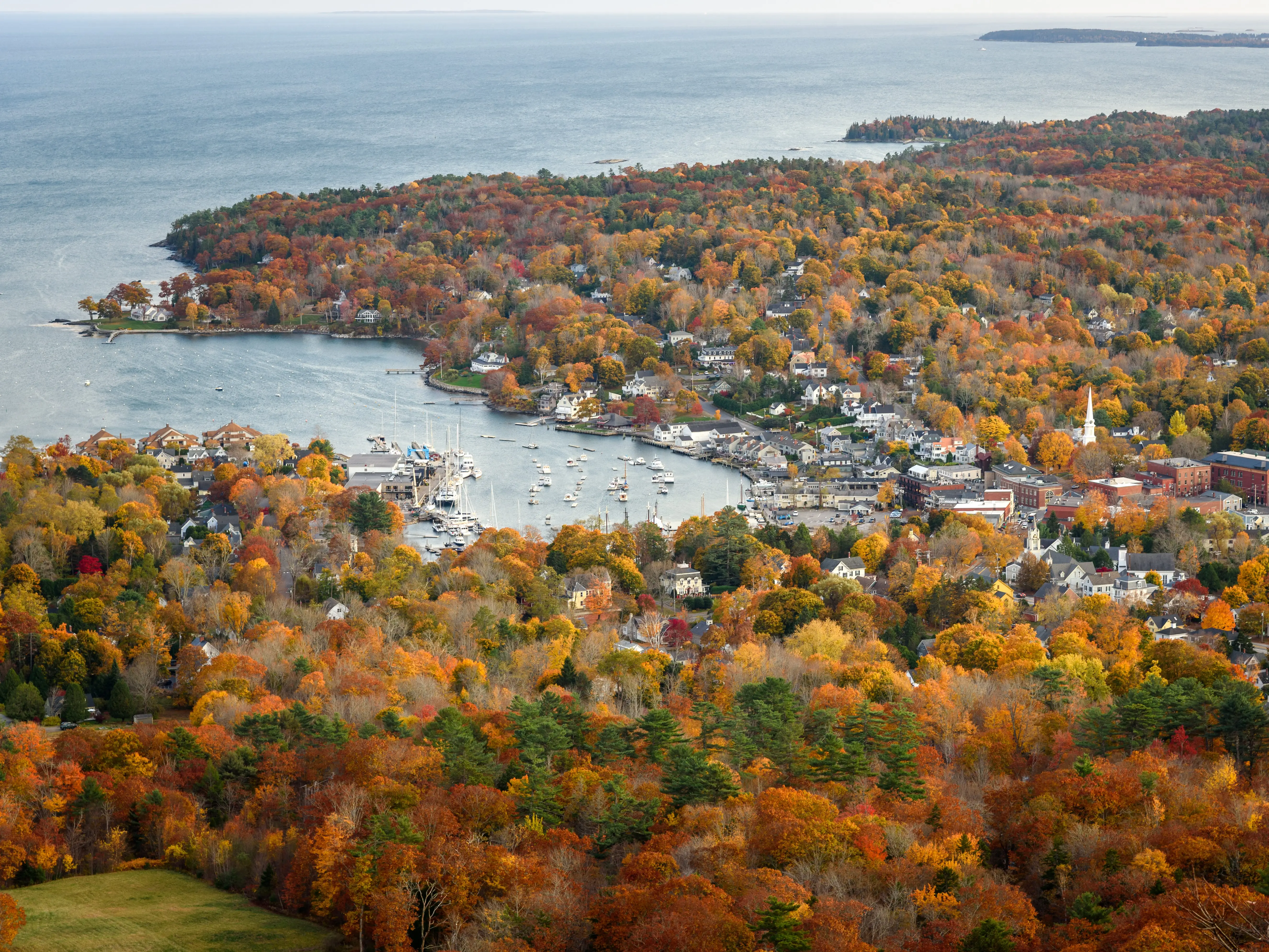 View of Camden and the forested coastline at the peak of fall foliage. Maine, USA.