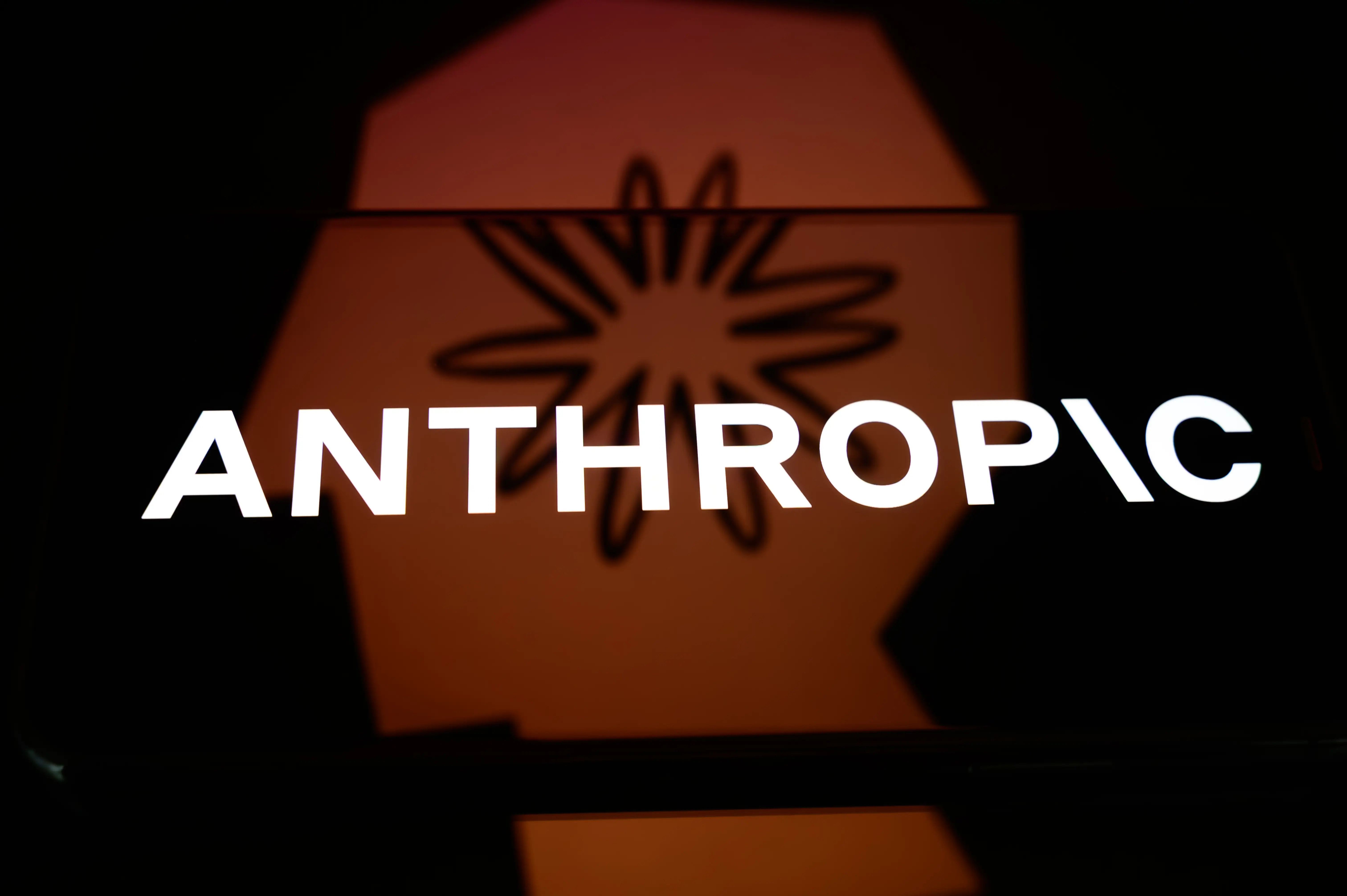 The Anthropic logo is displayed on a smartphone screen placed on a reflective surface onto which a company branding illustration is projected, in Creteil, France, on June 2, 2026.