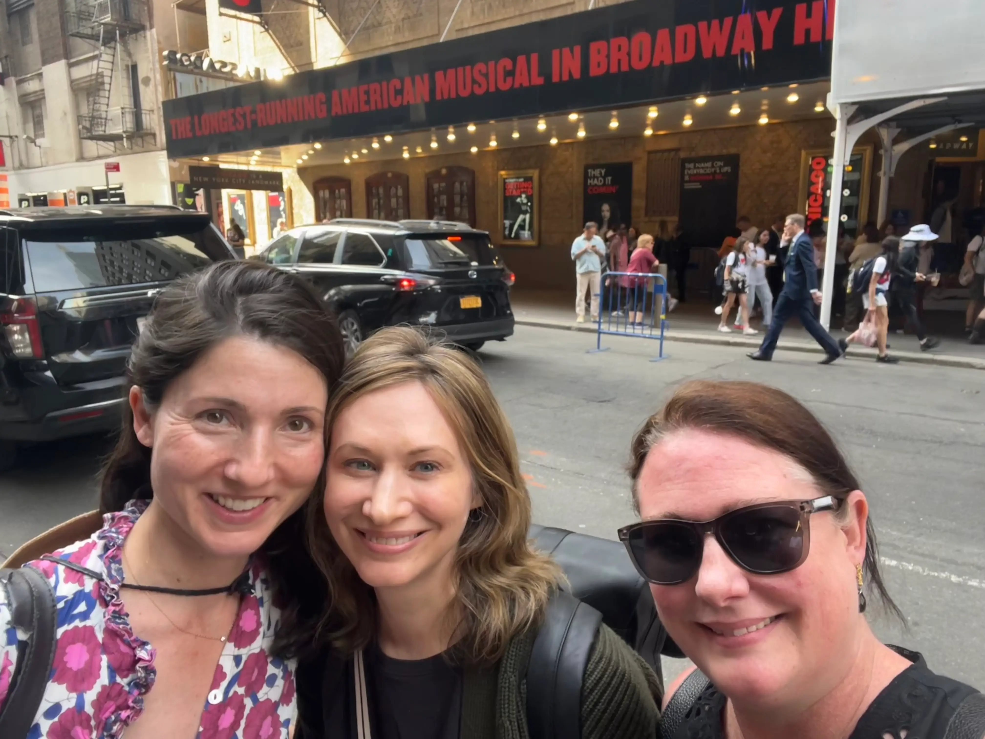 Three women take a selfie outside of the theater showing Chicago.