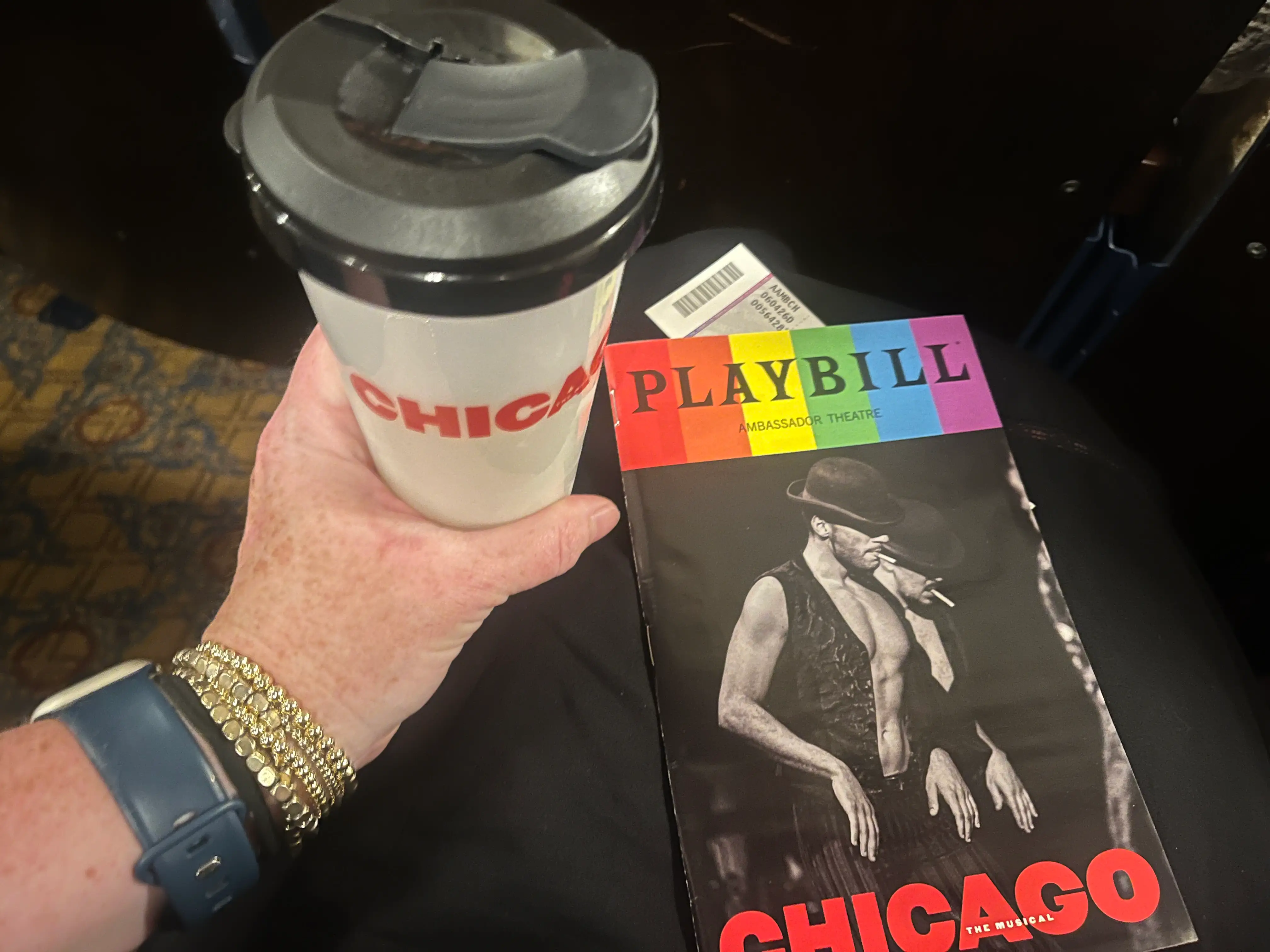 The author holds a cup and playbill while sitting in the audience for Chicago.