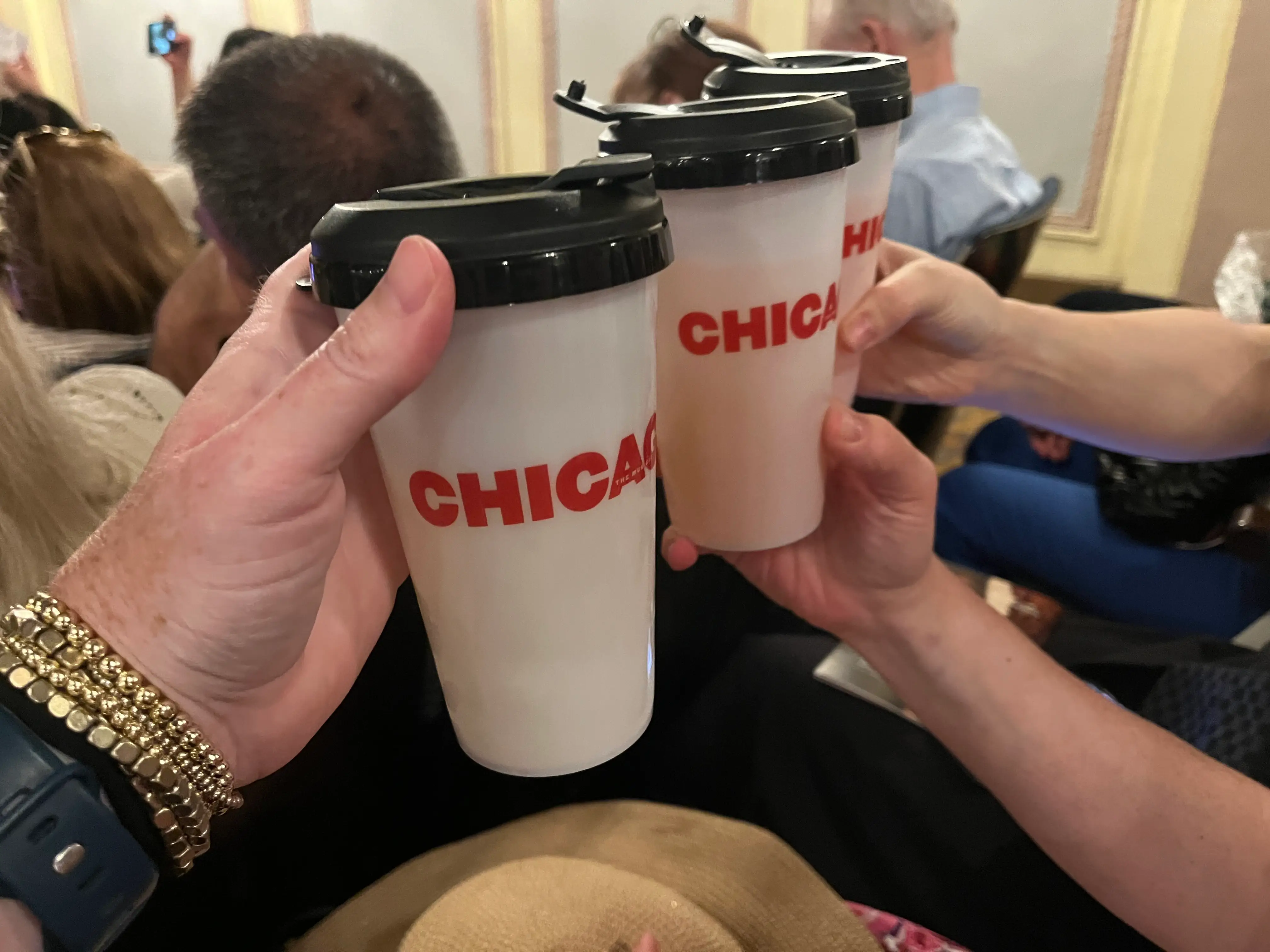 Three women cheers with Chicago-branded cups while sitting in the audience of a matinee.