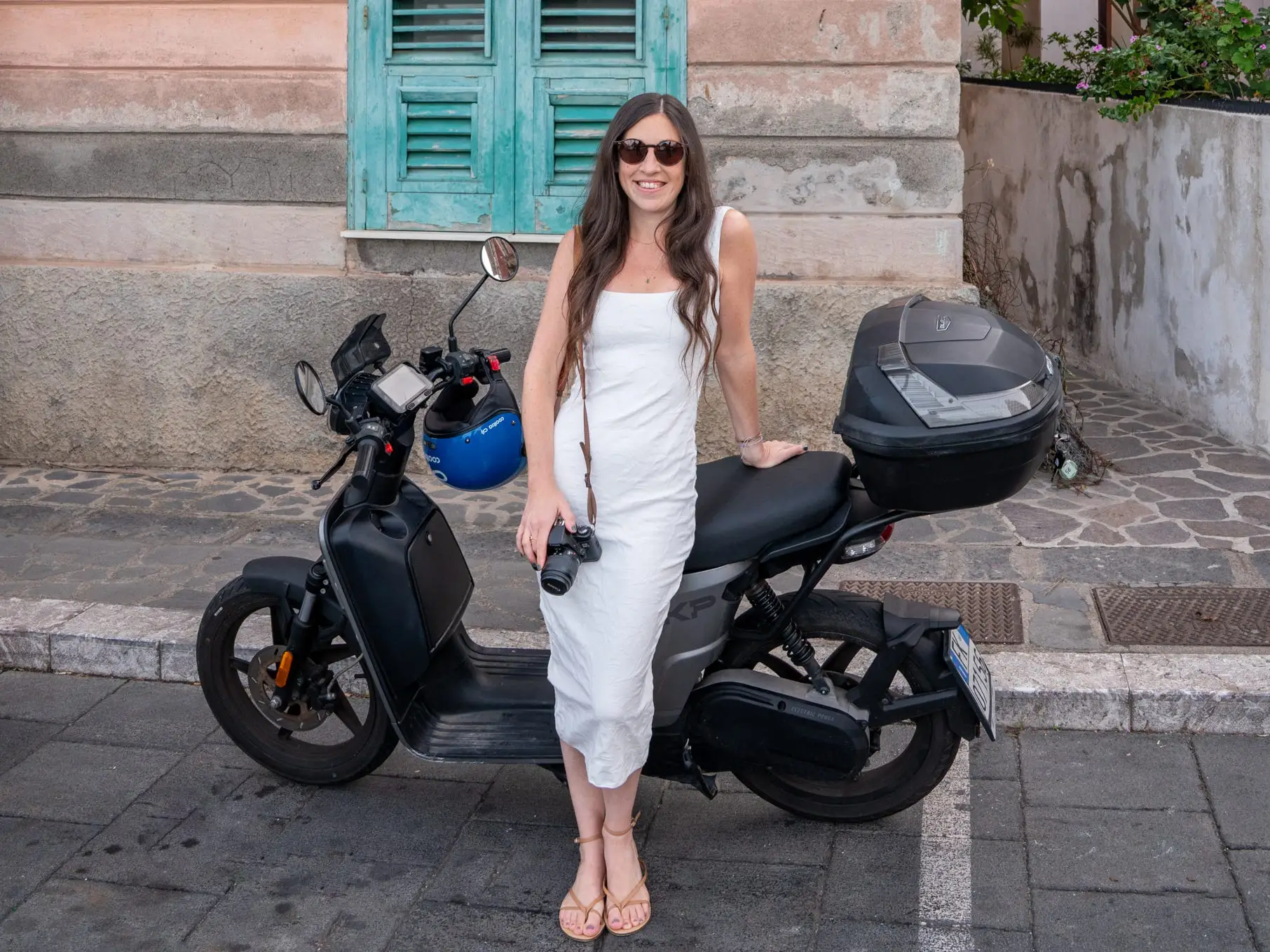 Woman in white dress and sunglasses posing near bike in Sicily