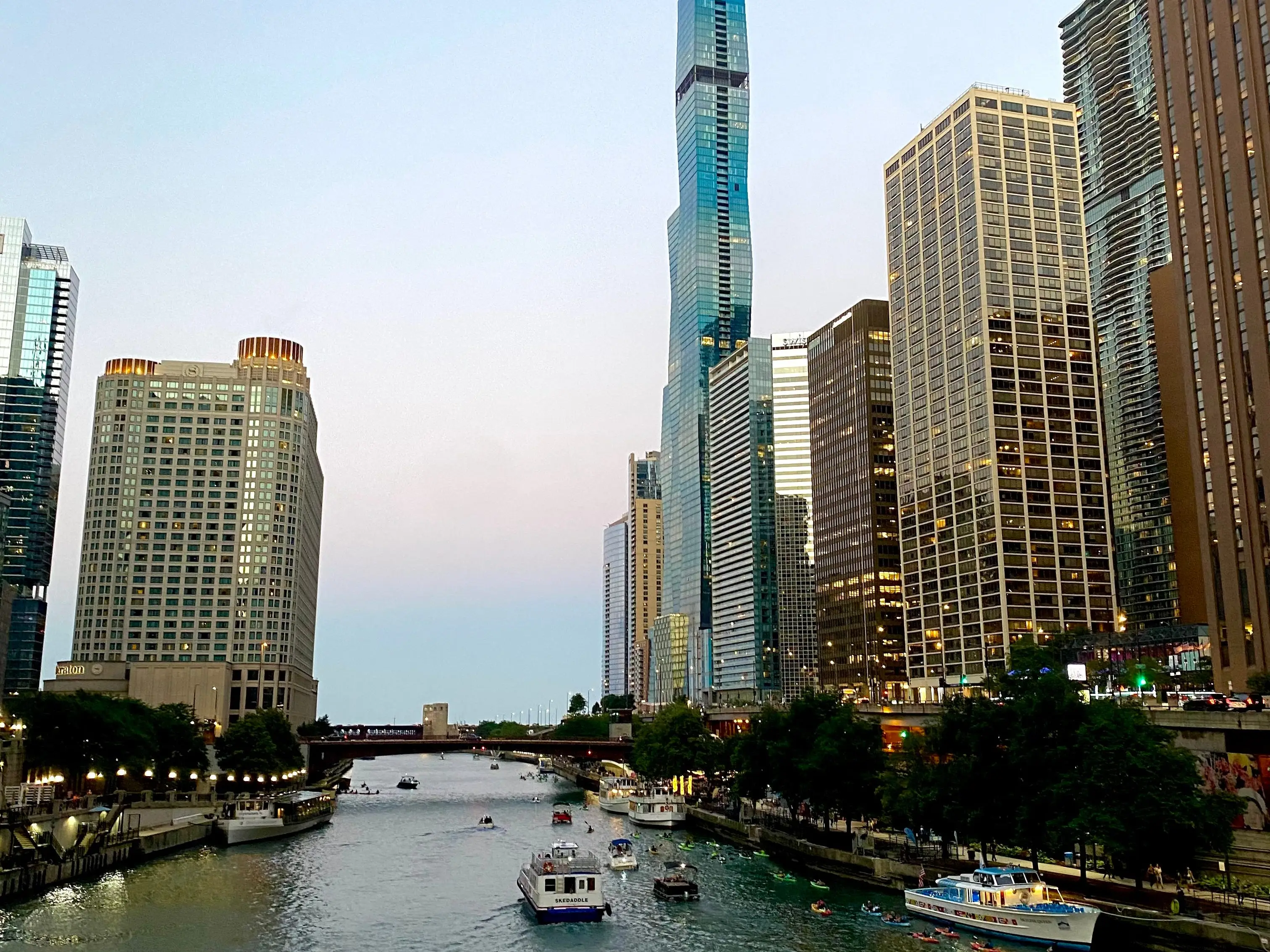 Several boats travel past countless buildings along the Chicago River.