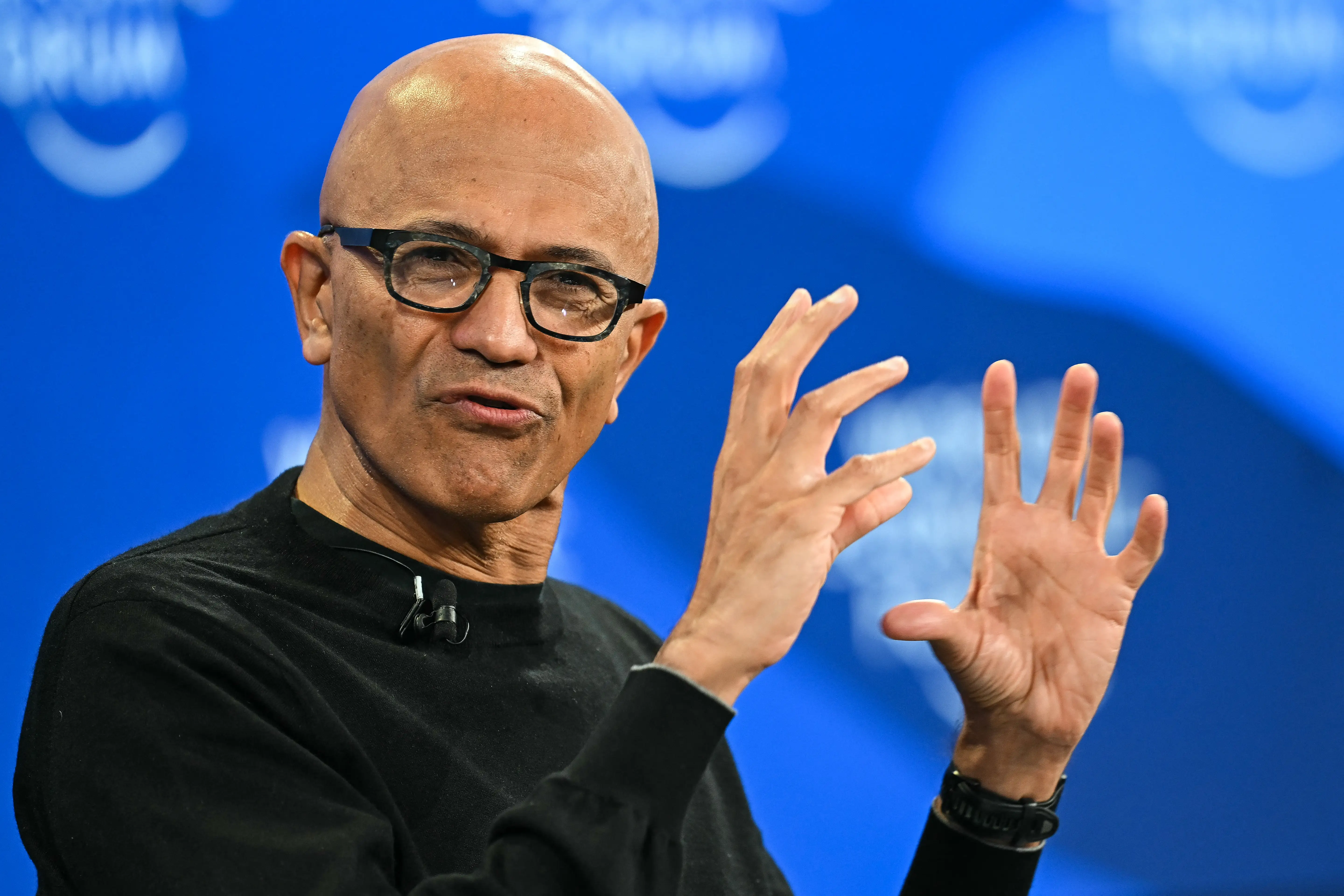 Microsoft CEO Satya Nadella gestures as he speaks while wearing glasses and a black sweater.