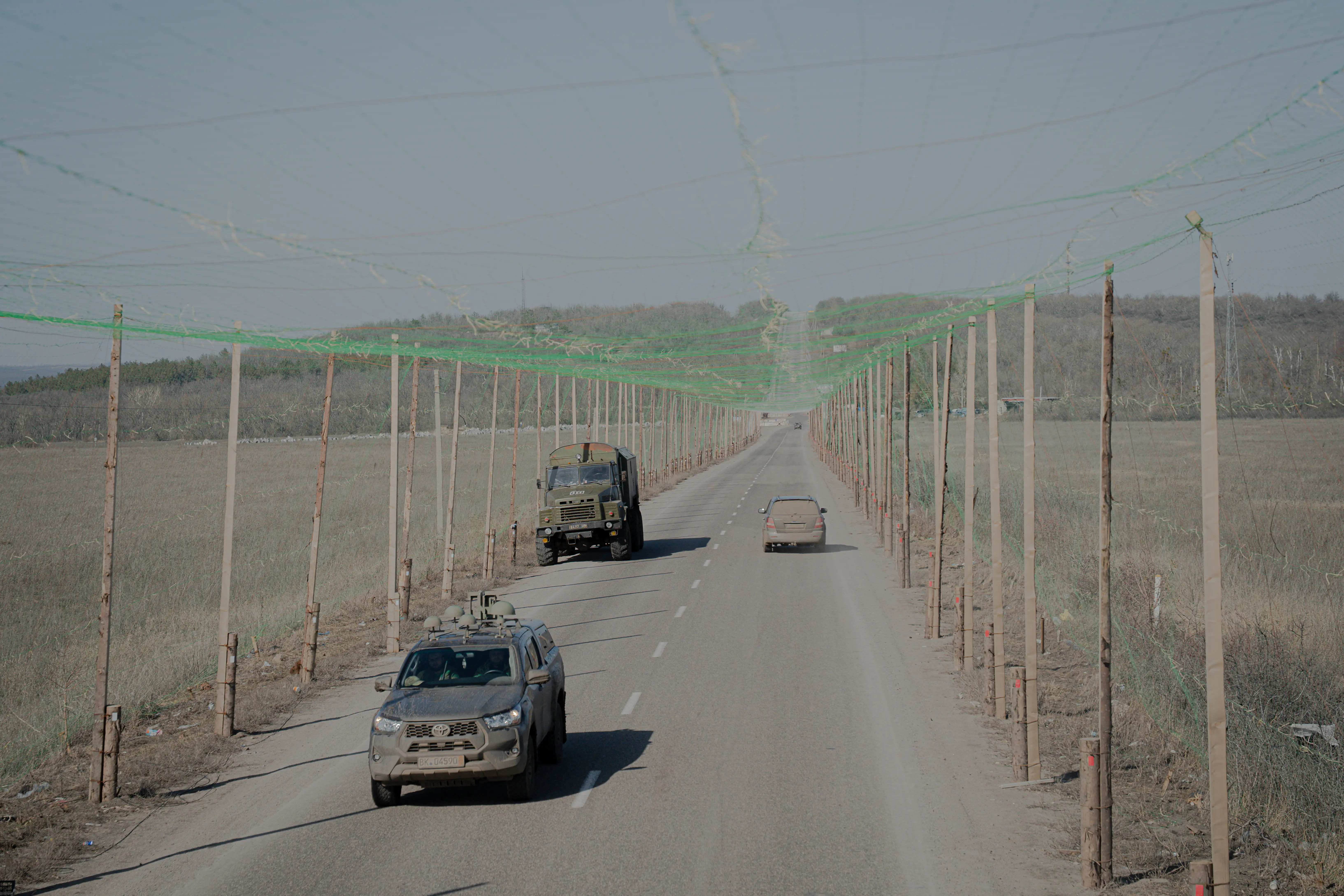 Ukrainian military vehicles driving down a road covered with anti-drone netting to protect against drone attacks in Kharkiv.