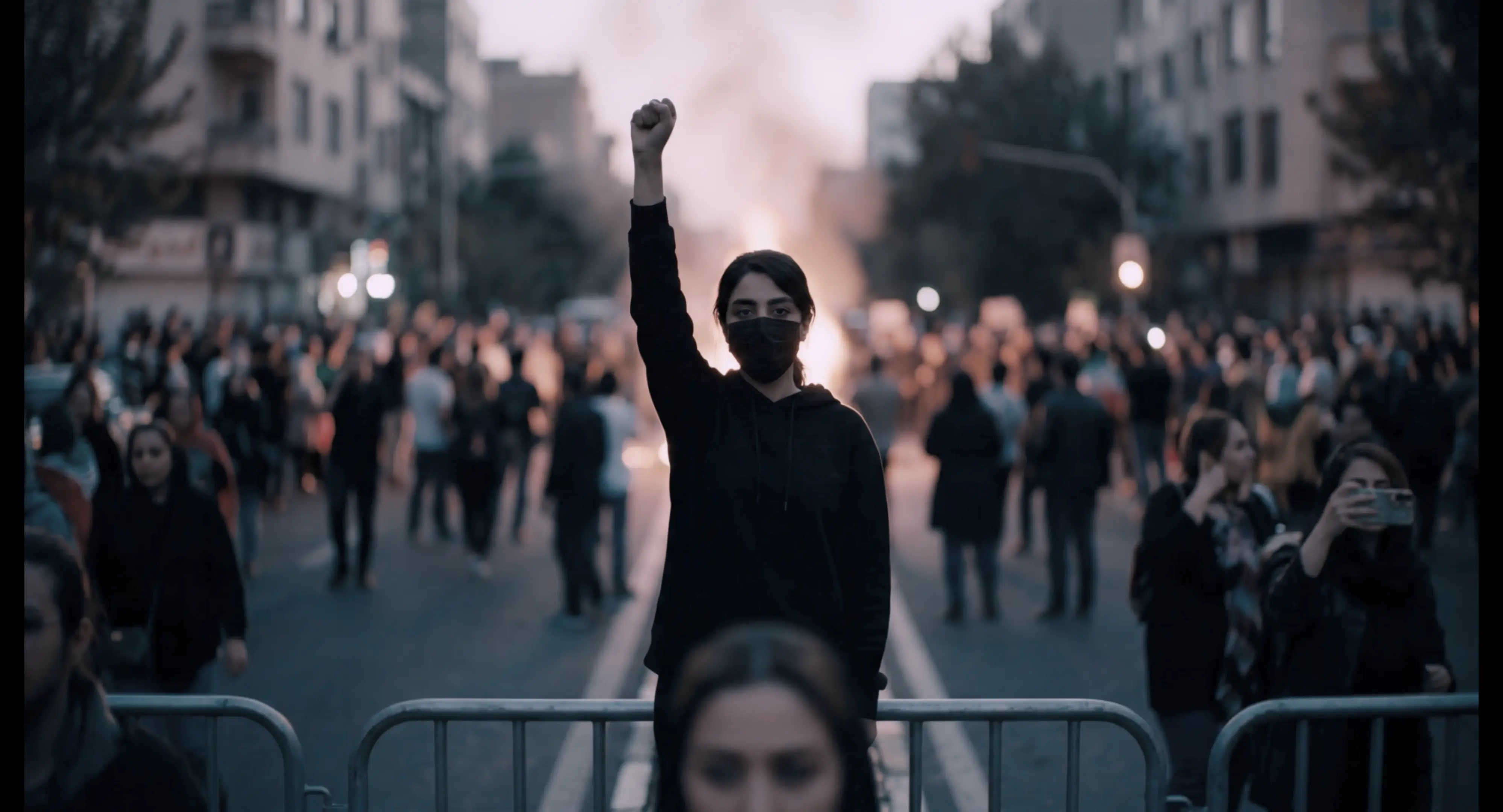 A protest scene, with a woman in the center holding her right arm up, hand in a fist