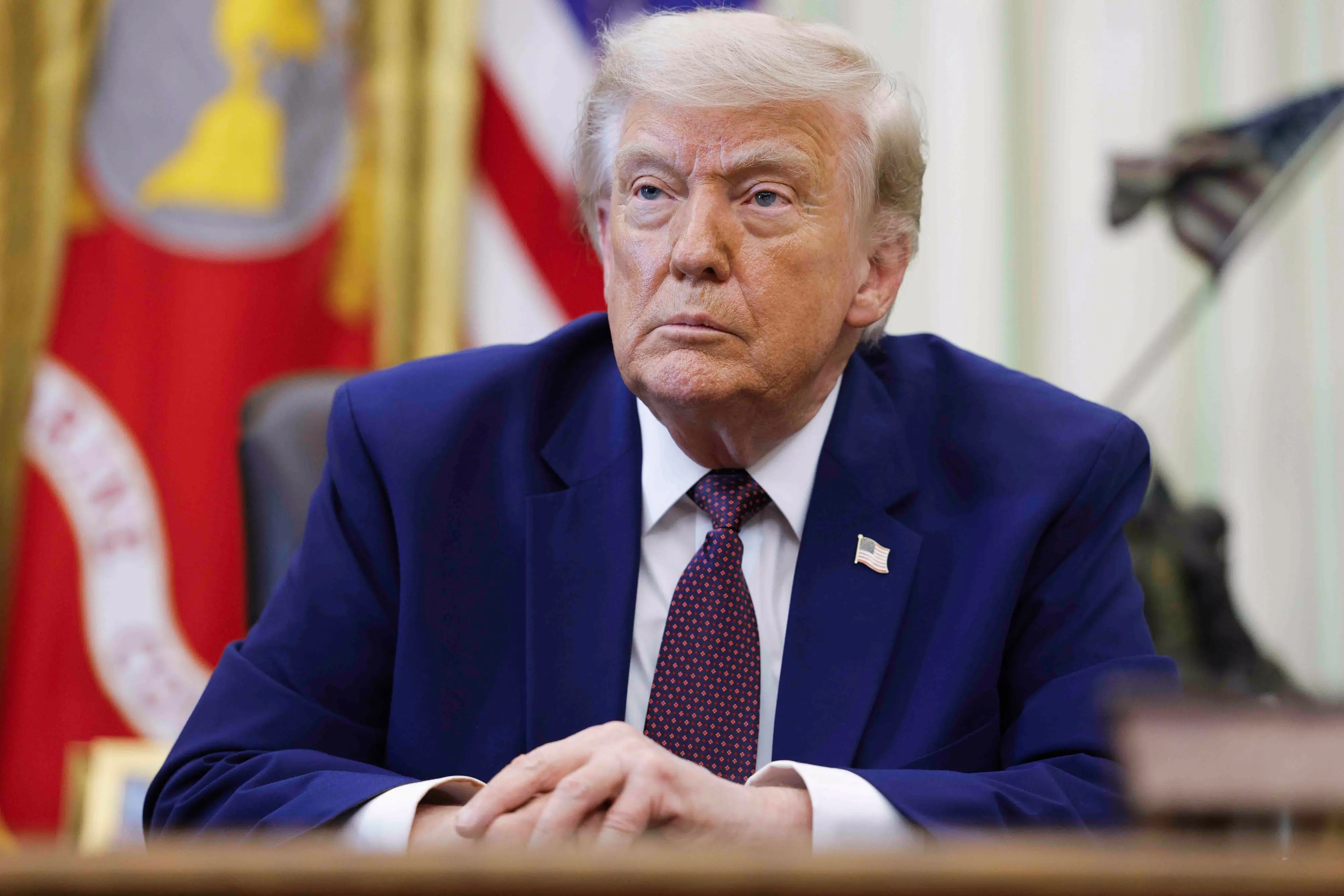 President Donald Trump sits behidn a desk with flags behind him