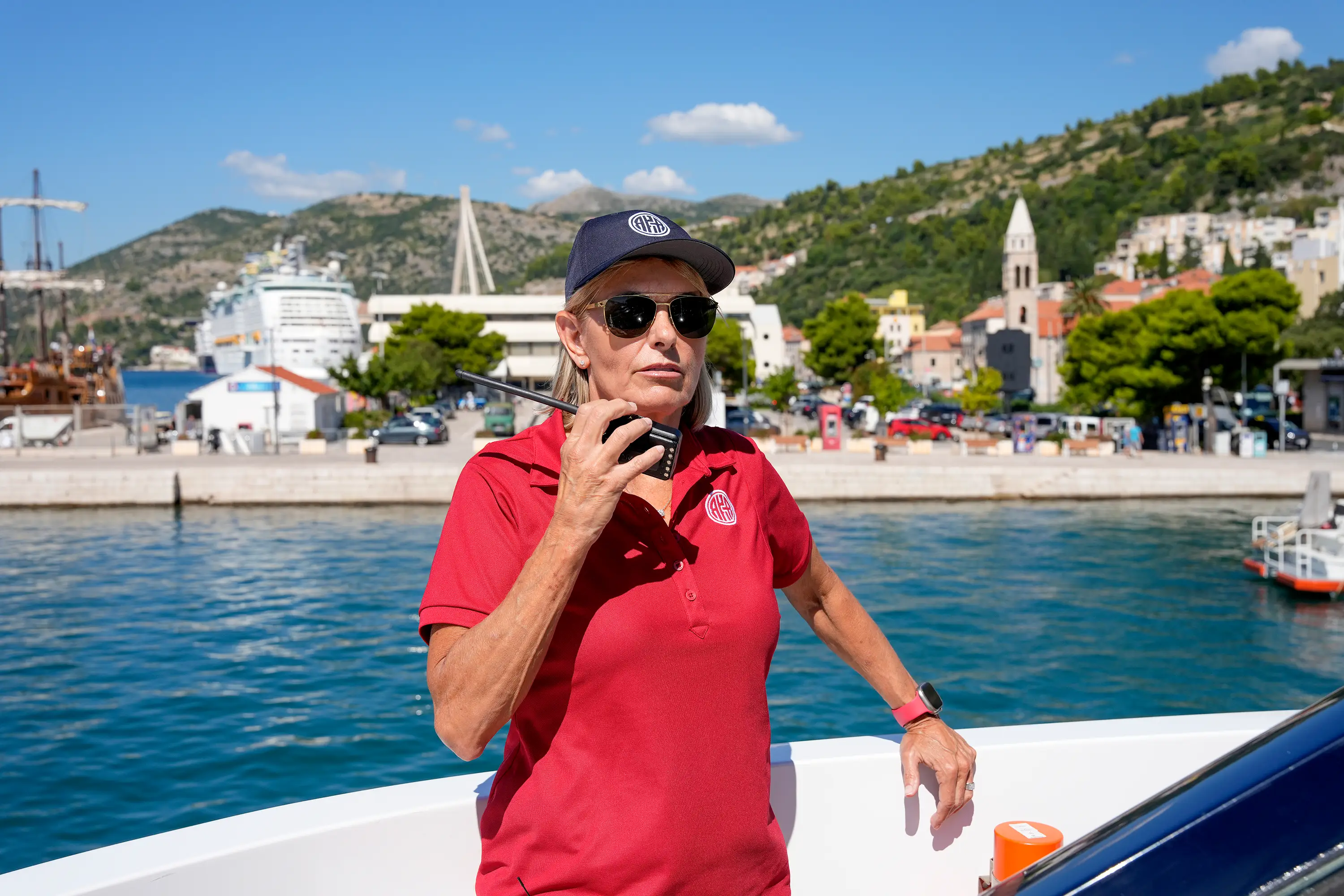 Captain Sandy Yawn wears a hat and sunglasses holding a radio on deck in Croatia.