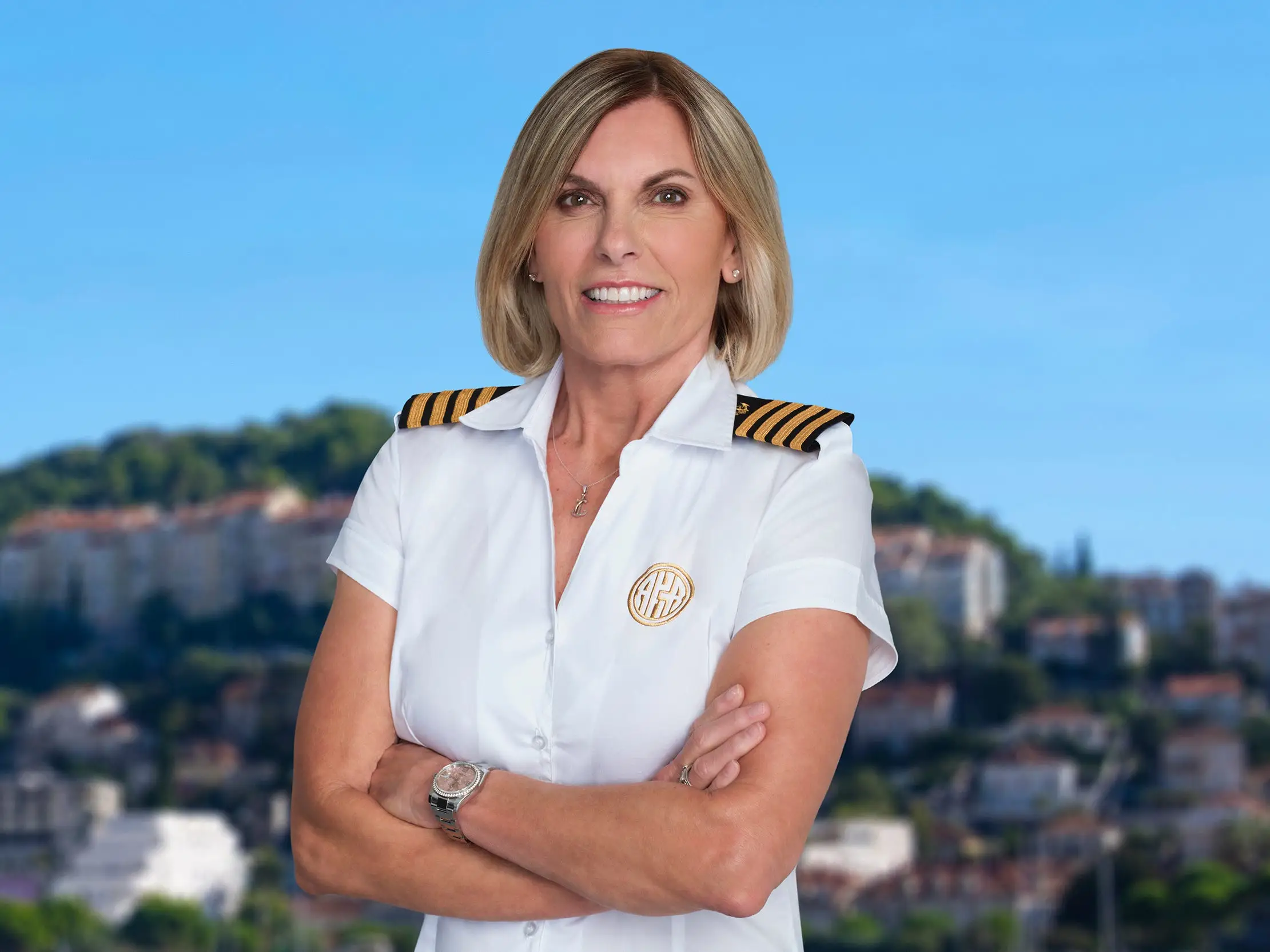 Captain Sandy stands on a dock in uniform with her arms crossed.