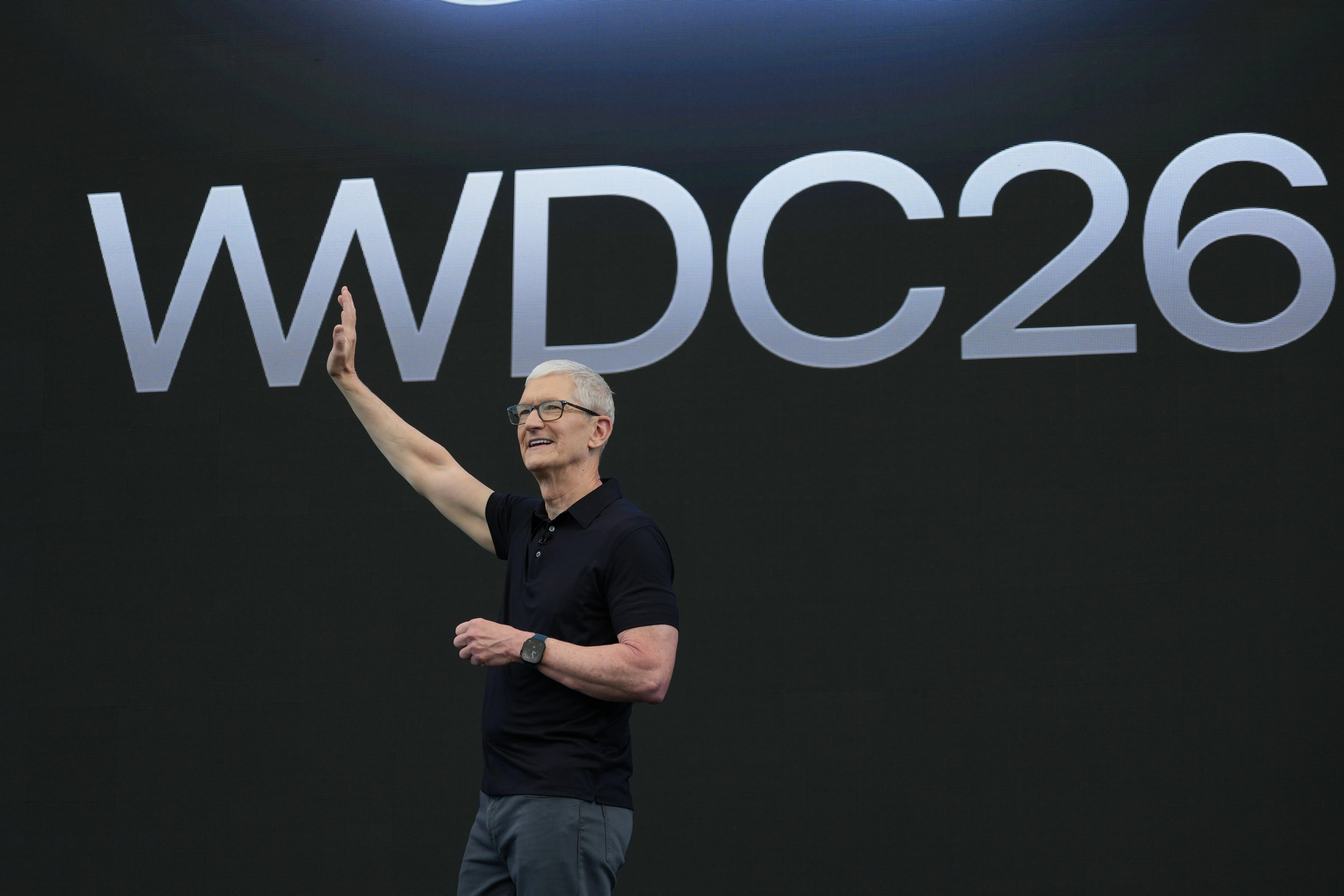 Tim Cook waves his right arm while standing on a stage with 