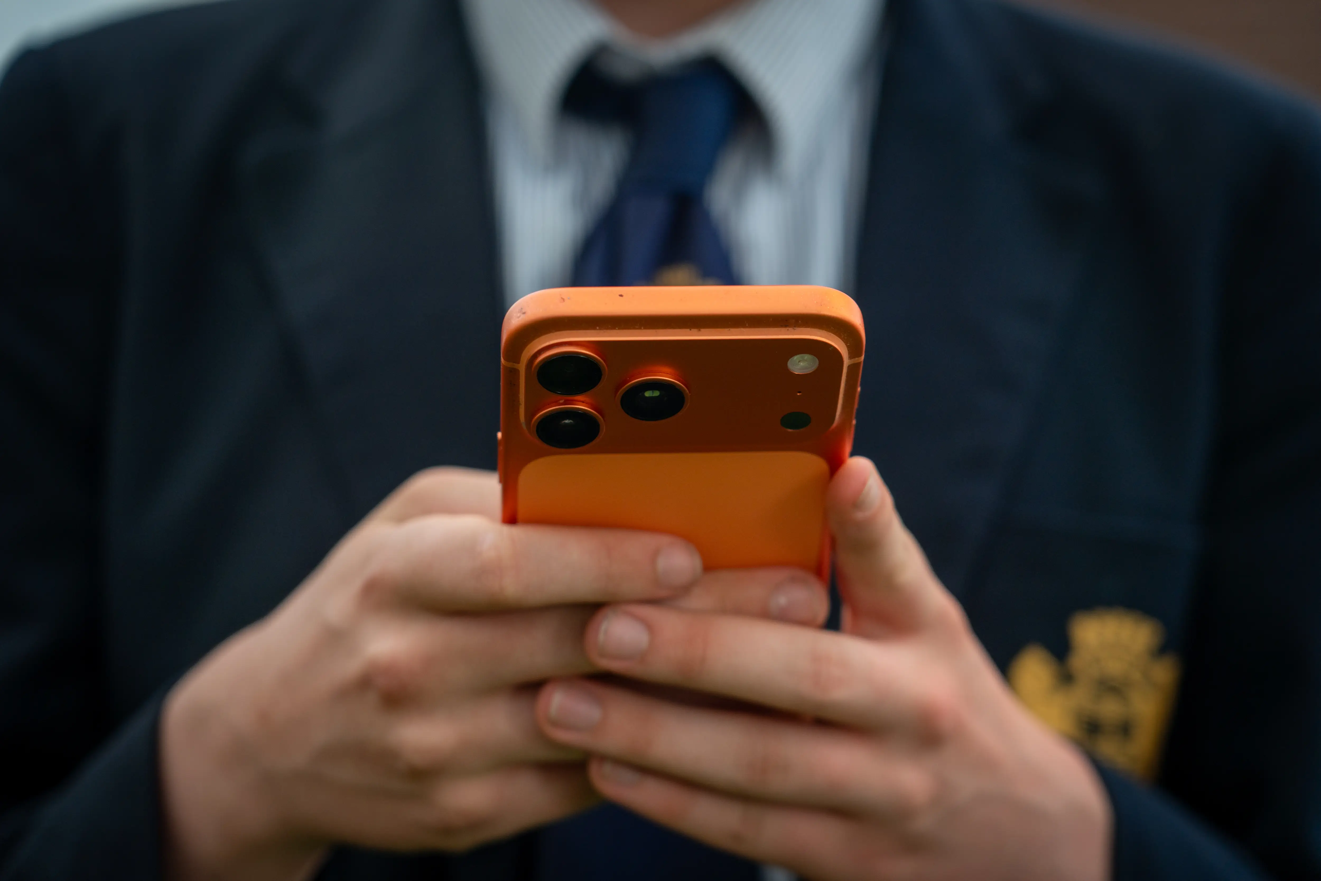A person wearing a blue suit and tie is holding an orange iPhone.