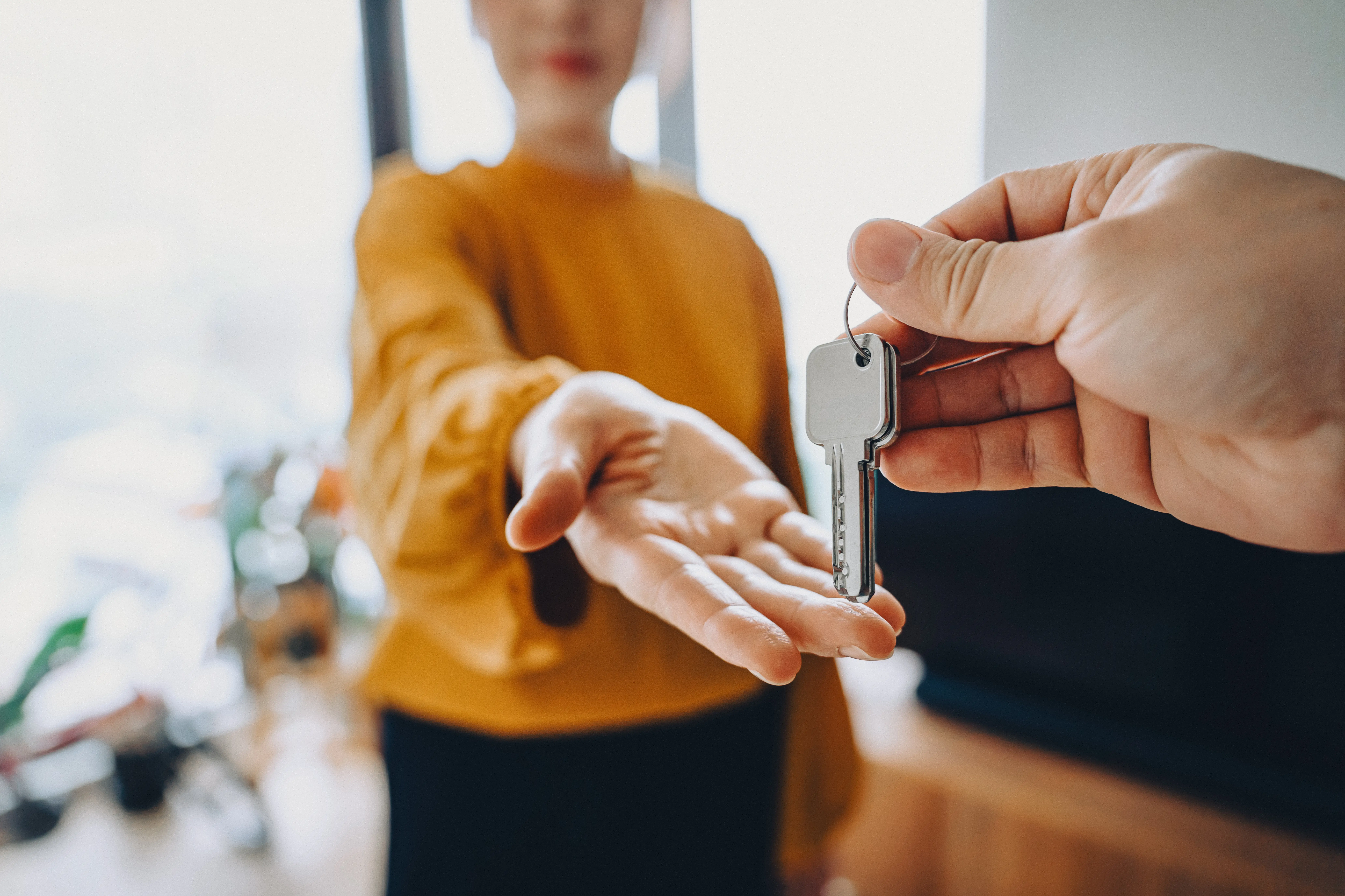 A woman's hand reaches out for a pair of keys being held by another person.