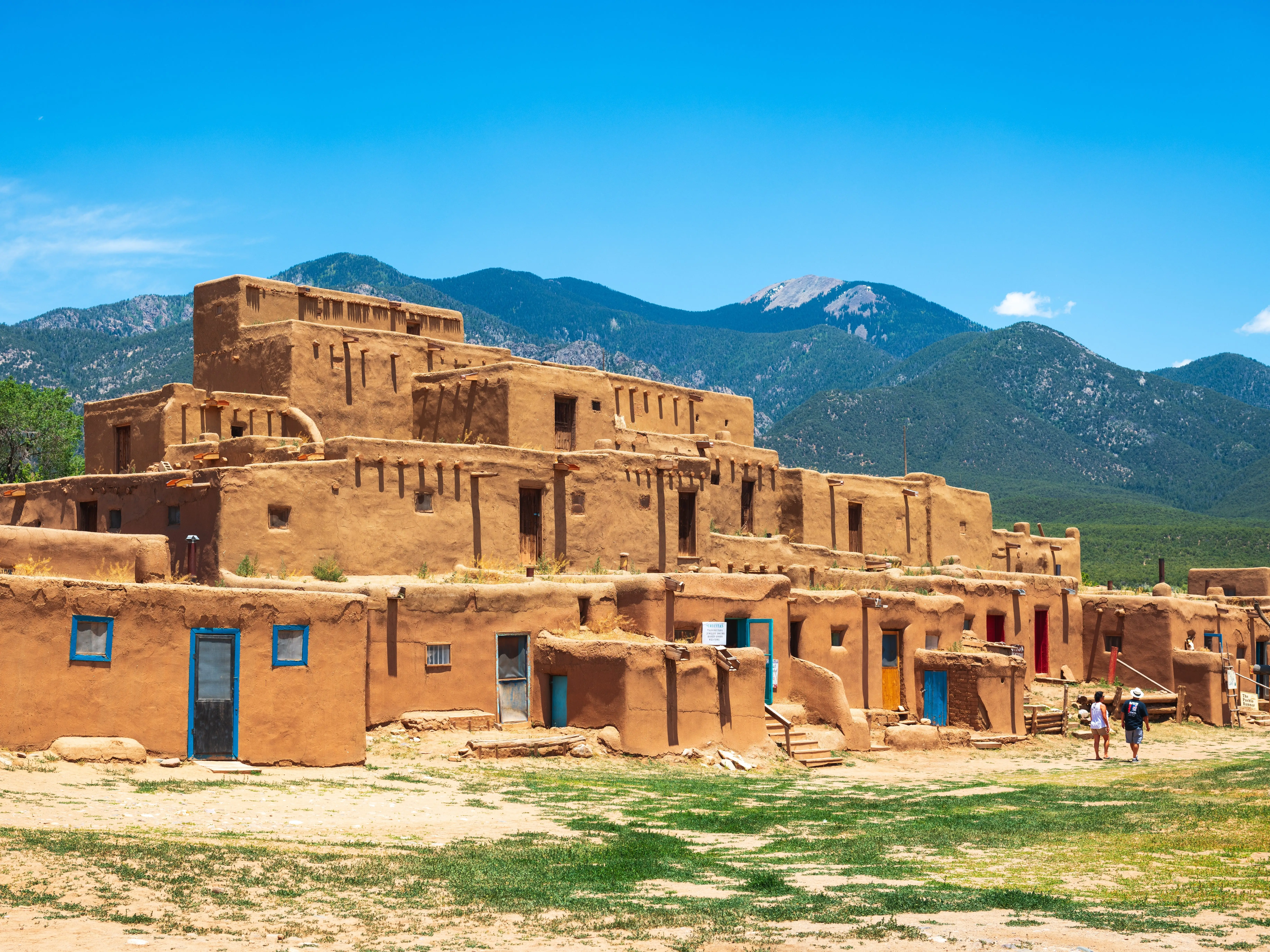 An Adobe-style building with blue doors at Taos Pueblo, with mountains in the background.