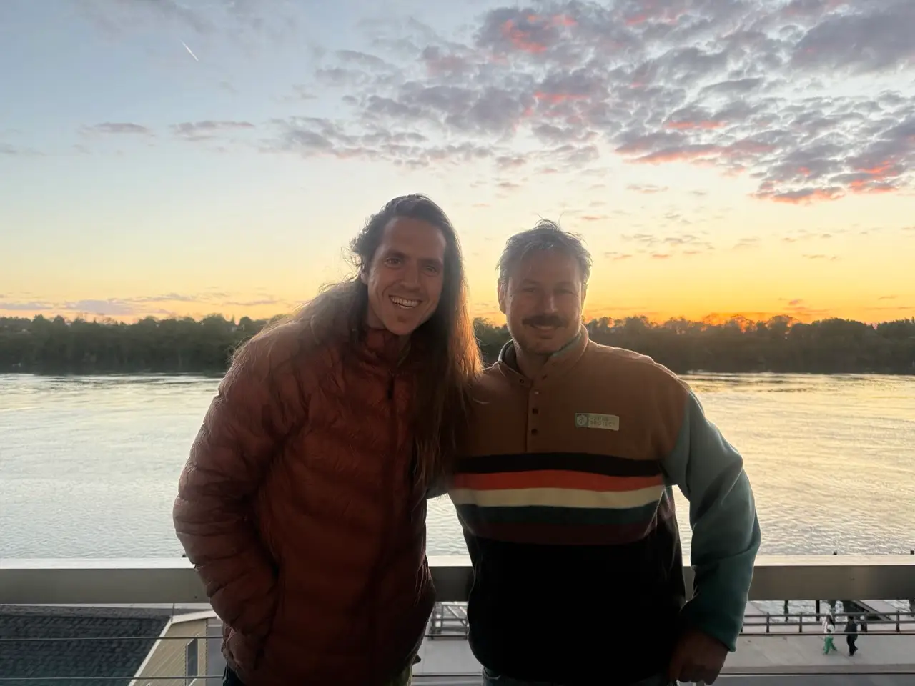 Two men smiling in front of sunset over water at Griffon in Lewiston