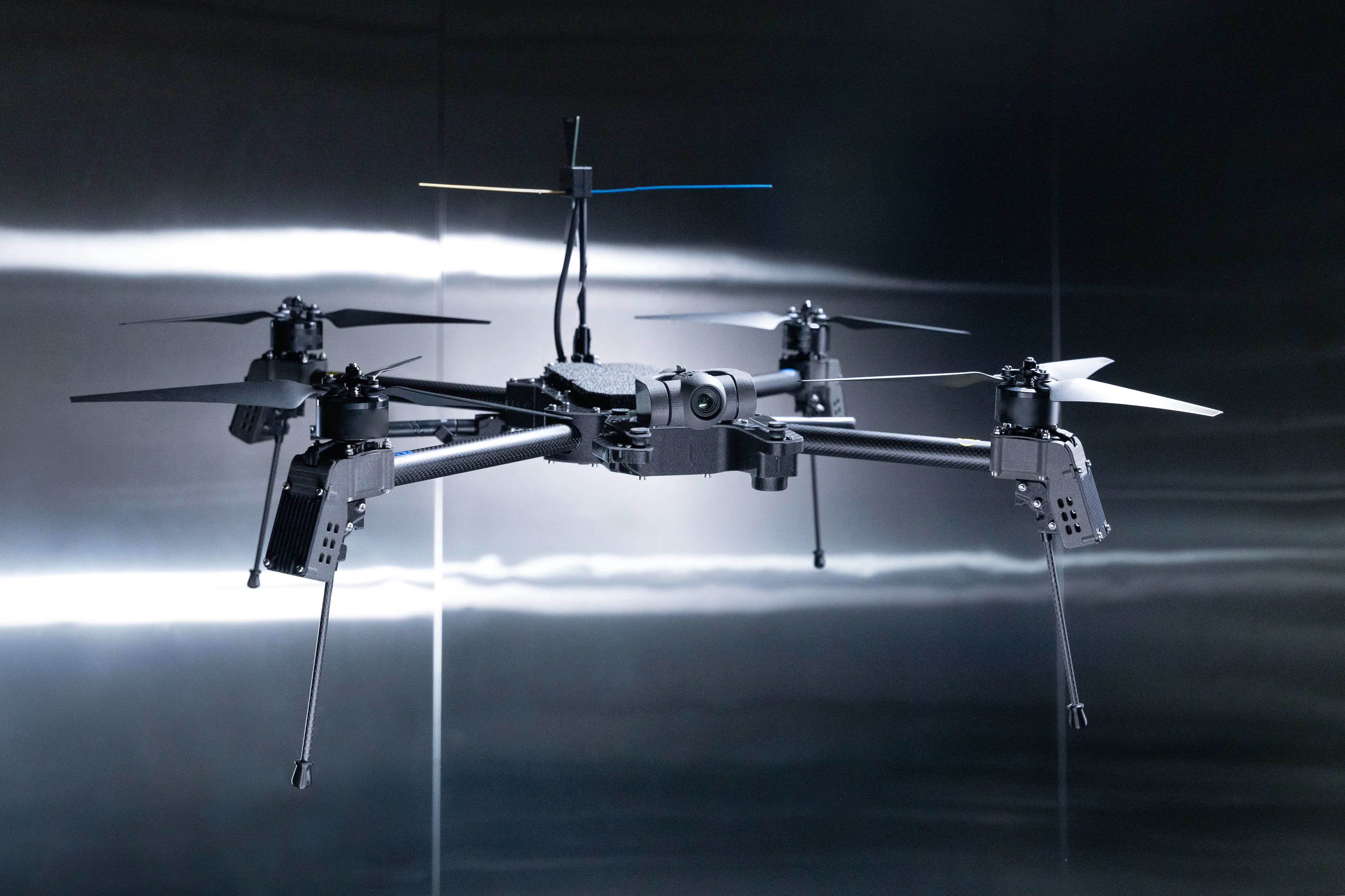 Quadcopter drone with camera and landing legs shown against a dark reflective indoor background.