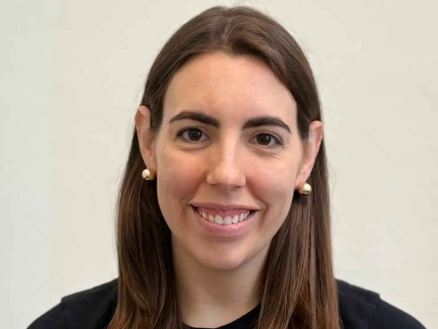 Smiling person with shoulder-length brown hair wearing a black top against a plain light background.