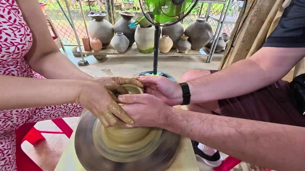 Two people shape wet clay together on a spinning pottery wheel in a ceramics workshop.