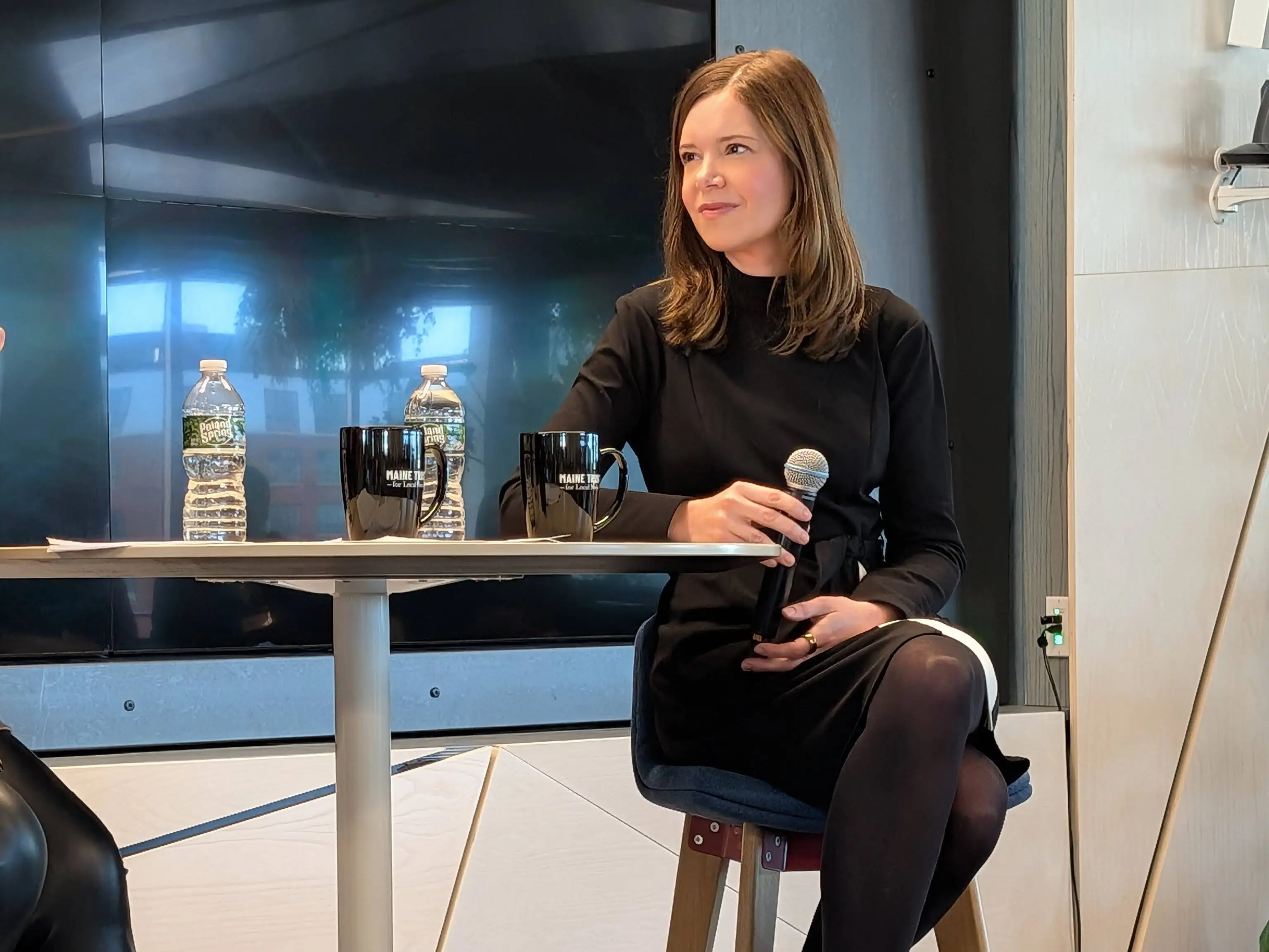 A woman wearing black is sitting at a table holding a microphone.