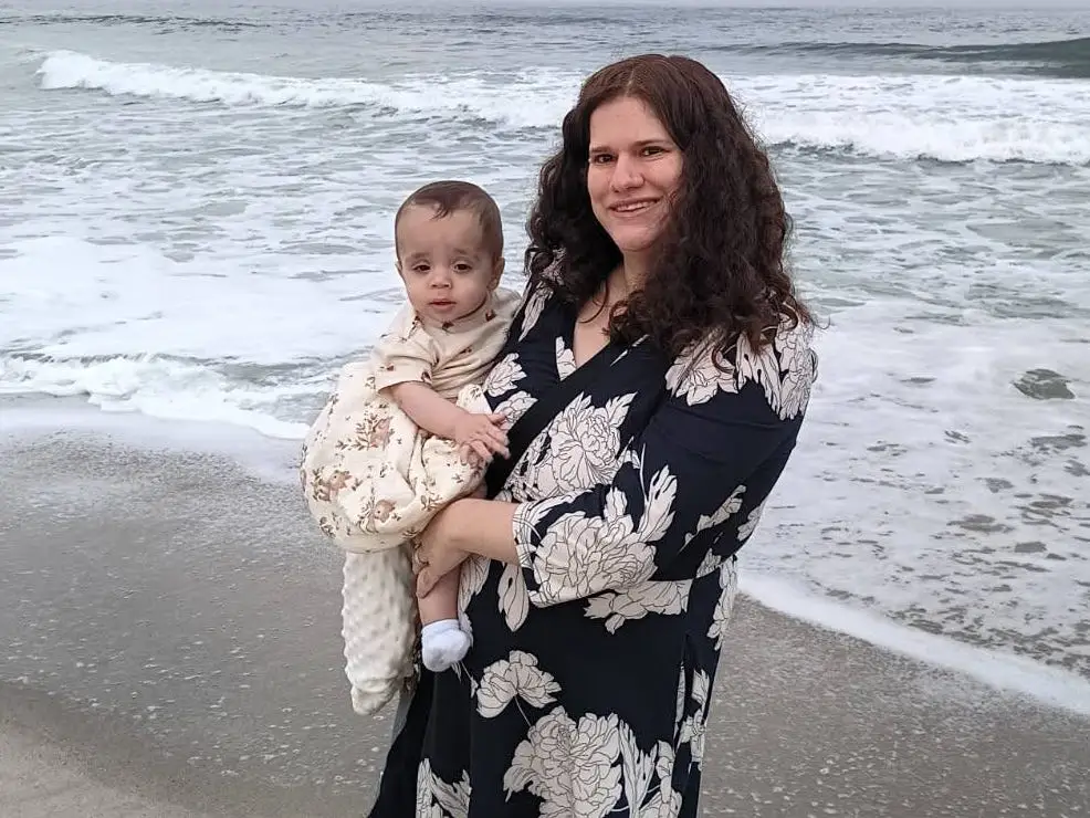 Ariel Goldstein holding her baby in front of the ocean