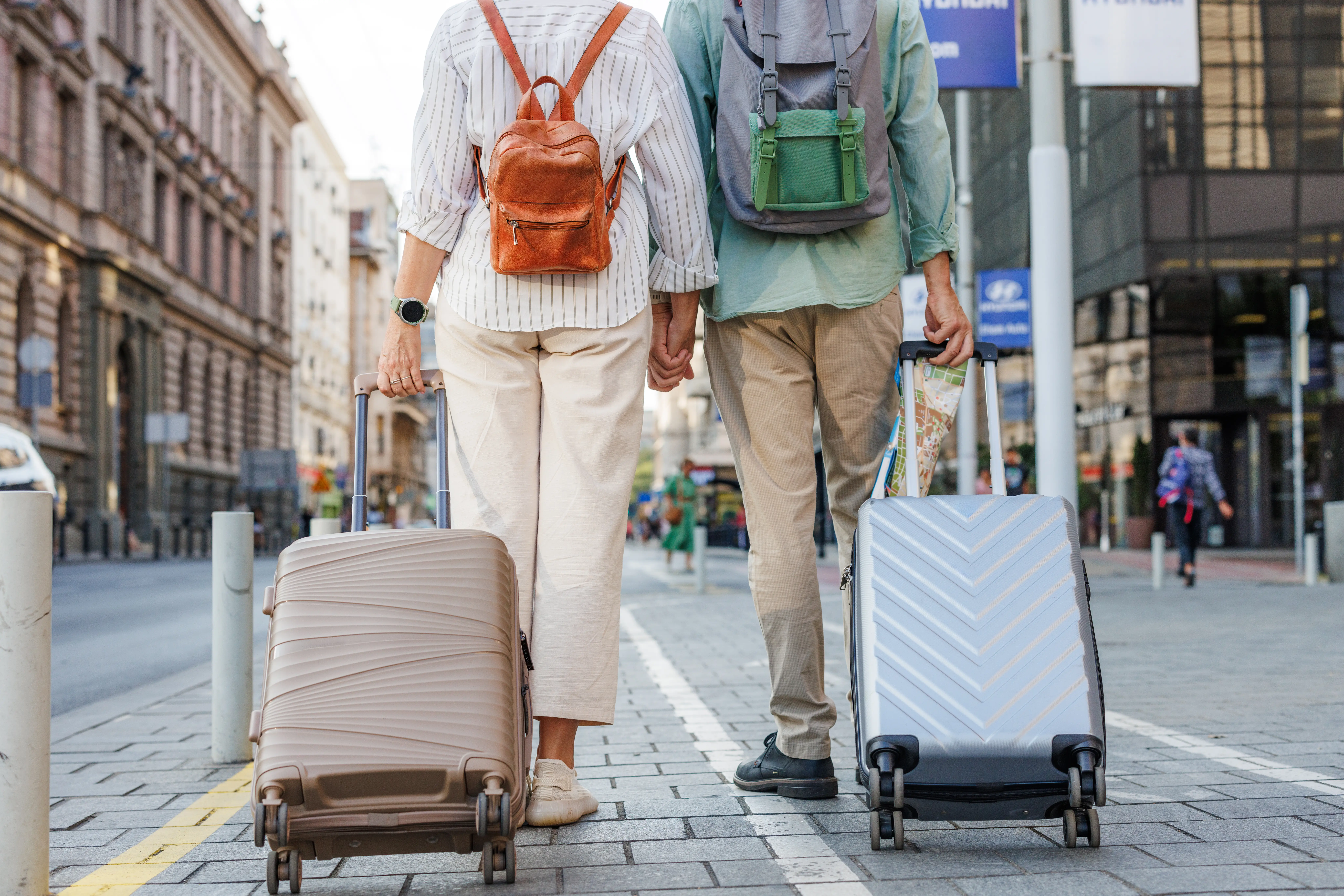 Two people with backpacks, suitcases walking down stone road