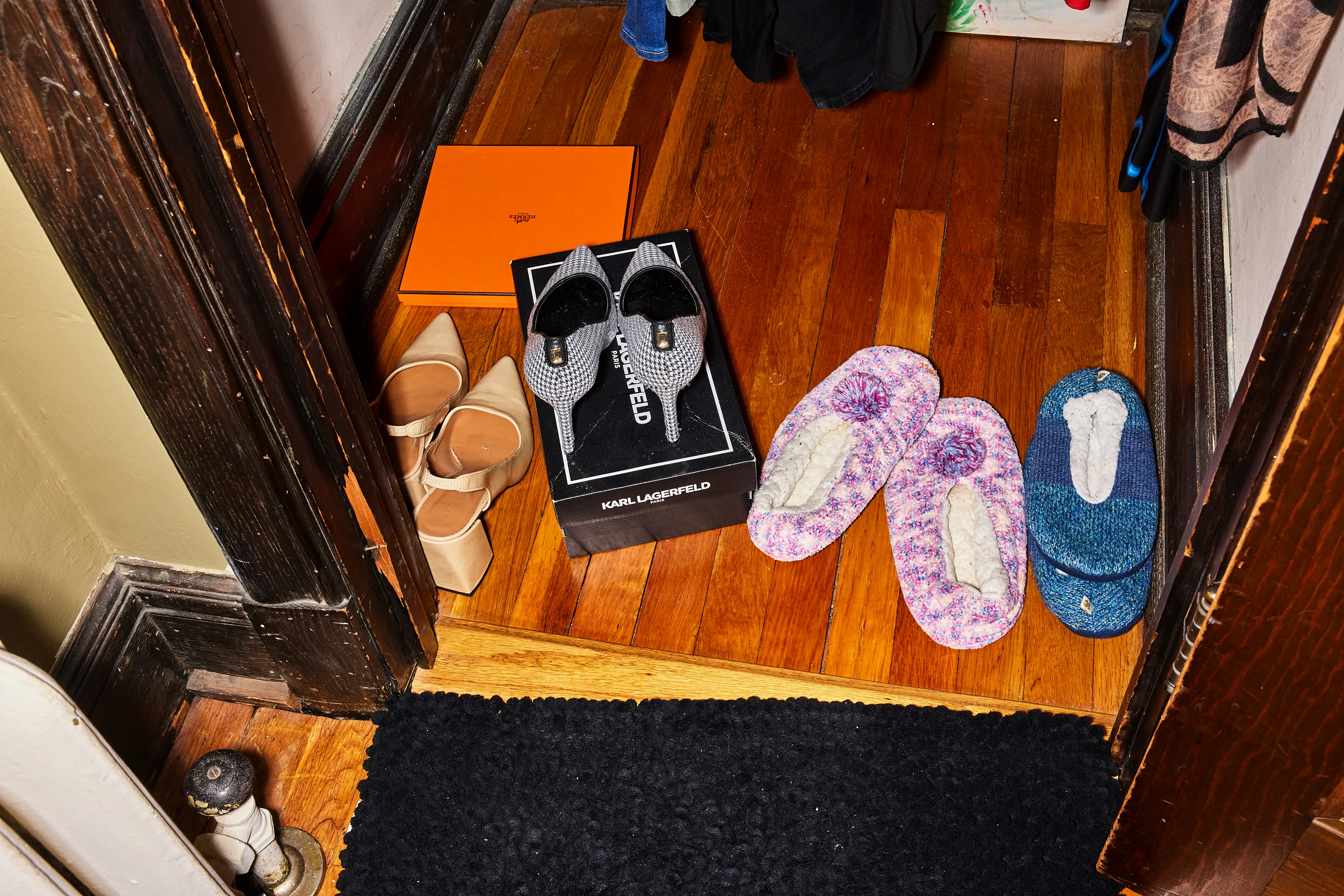 Assorted shoes and slippers sit on a wooden floor near a doorway beside a KARL LAGERFELD box.