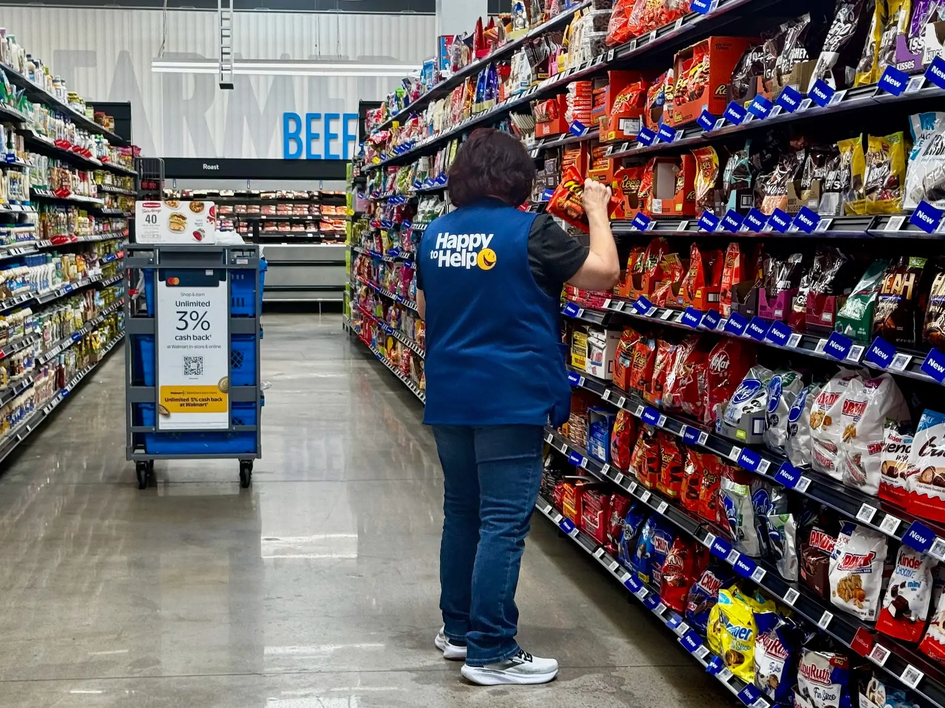 Store employee picks an order from candy and snack shelves in a brightly lit grocery aisle.