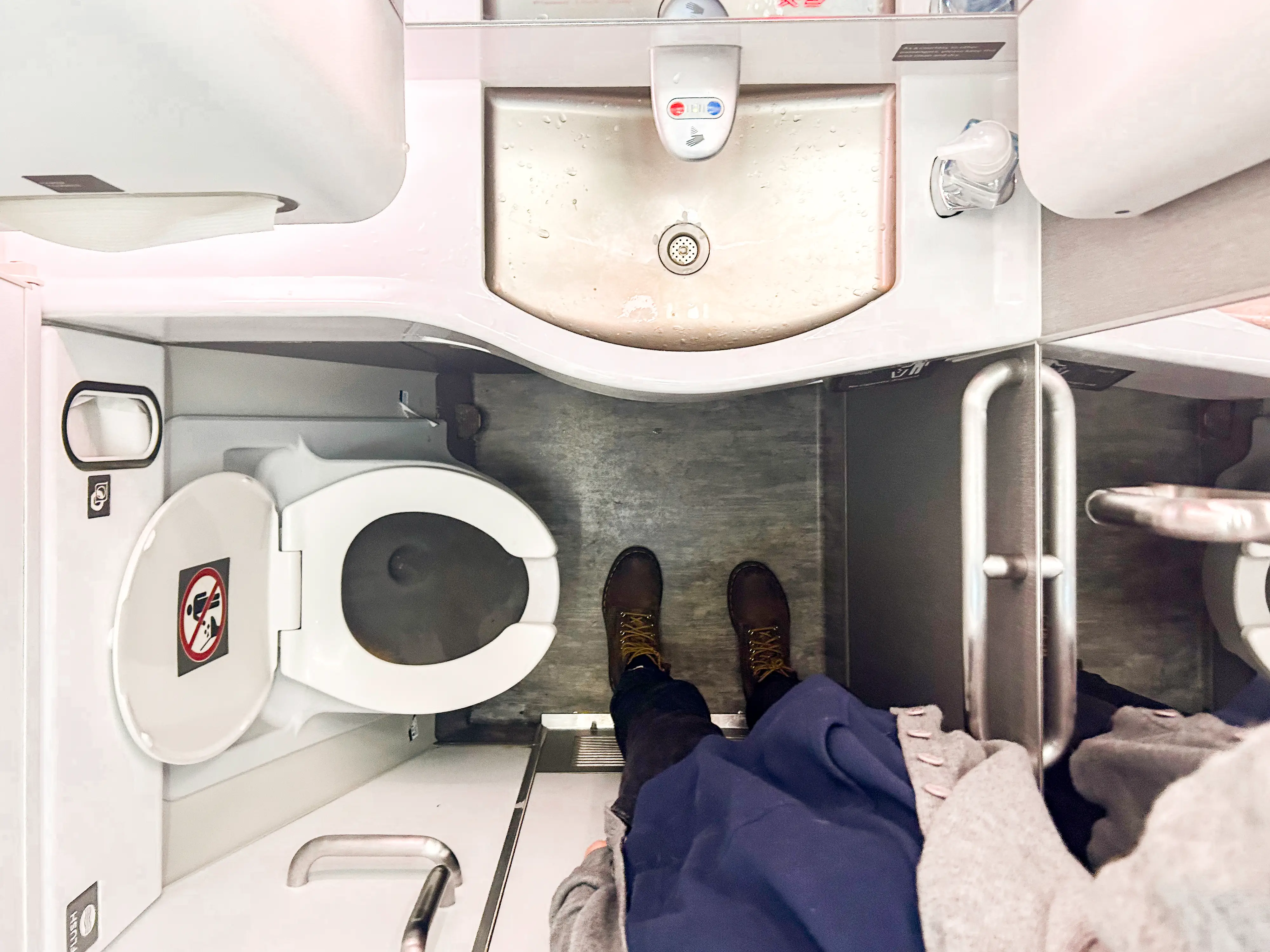 An aerial view of an airplane bathroom with a toilet on the left, a sink in the middle, and a door on the right