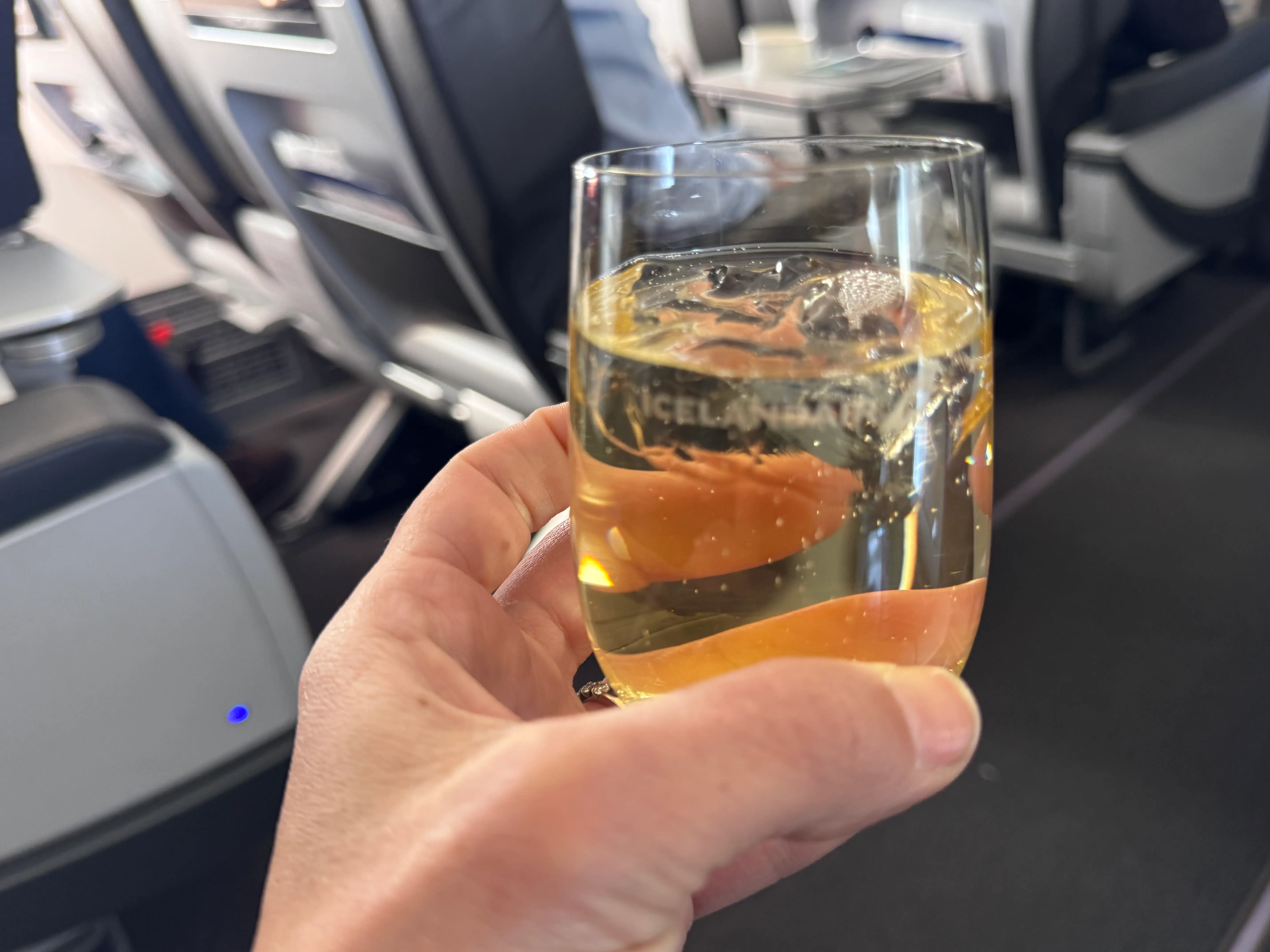 Hand holding glass of alcohol  on IcelandAir plane