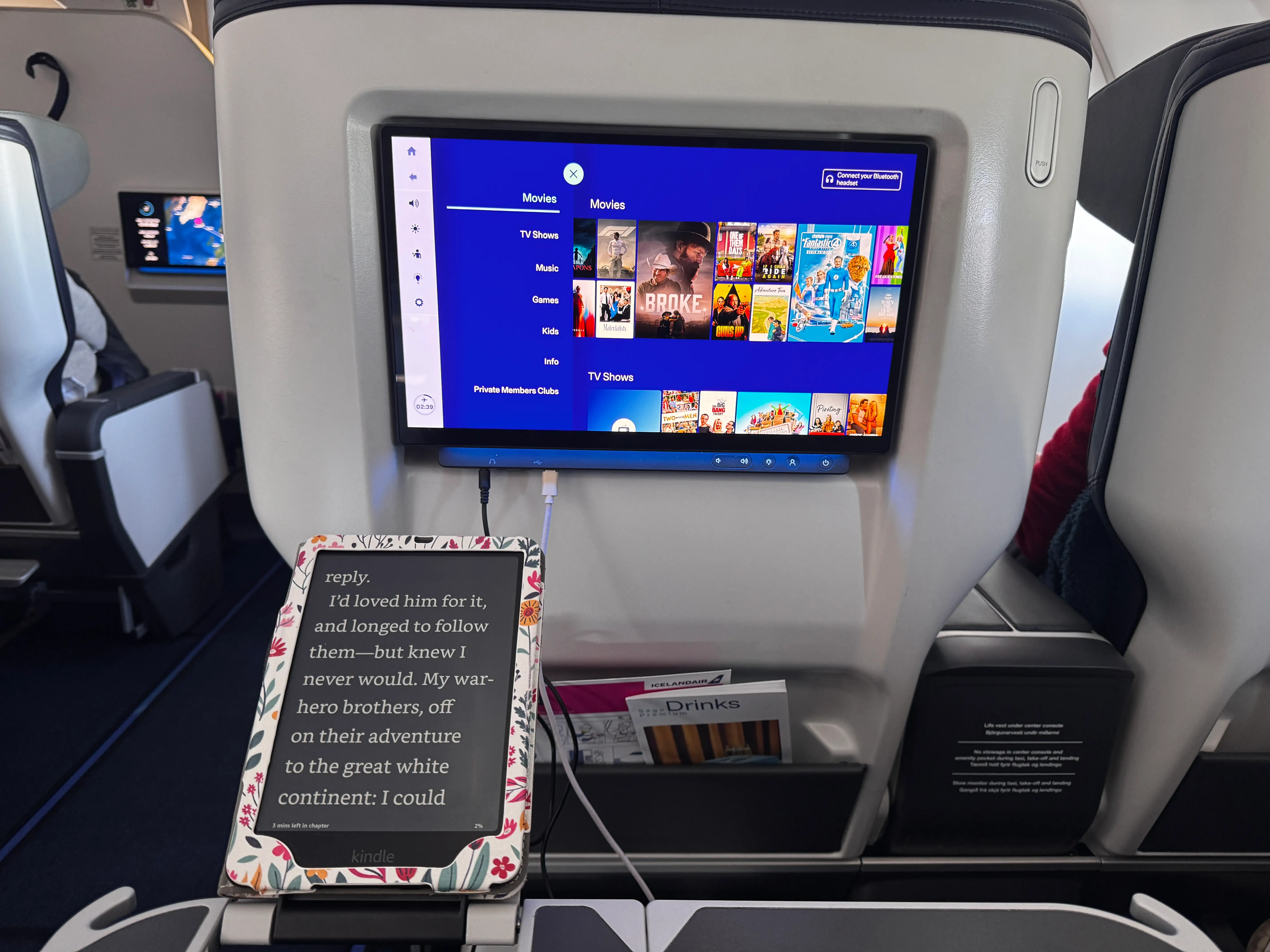 Hand holding e-reader in front of seatback screen in Saga Premium flight on ICelandair