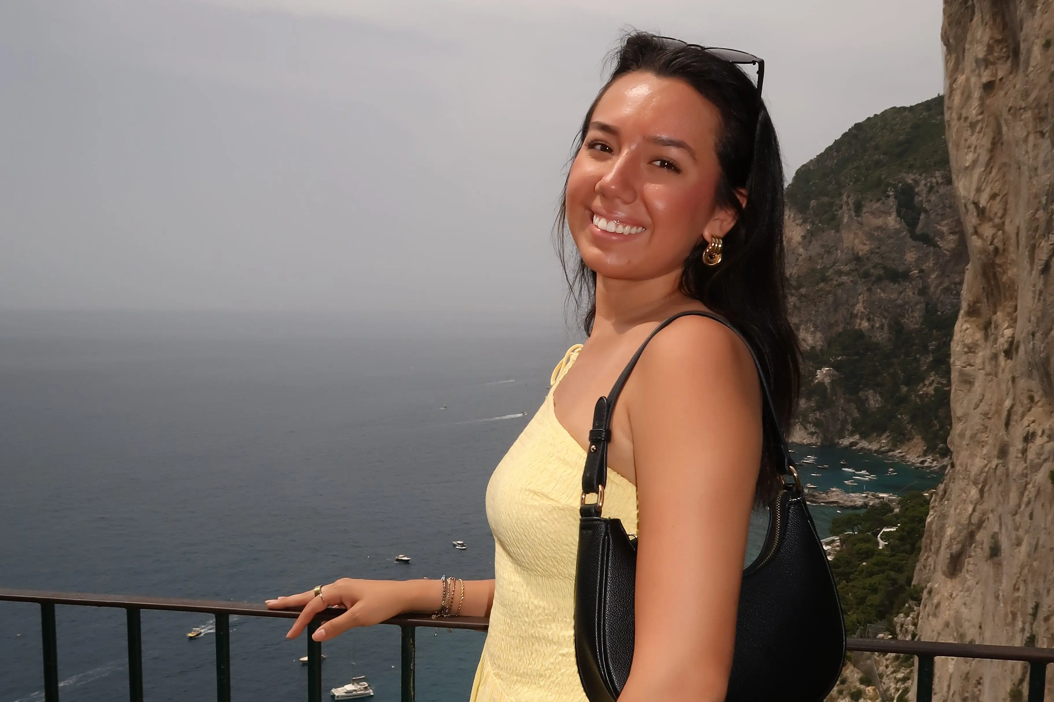 A woman smiling near a rail overlooking a mountain and the sea.
