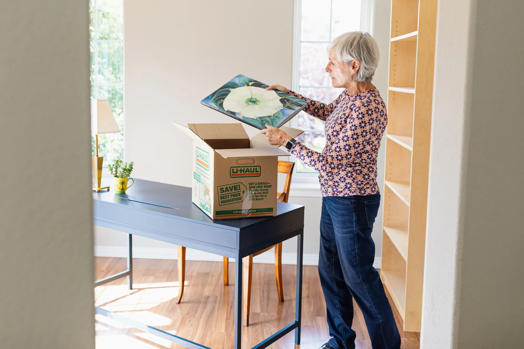 A woman packing a moving box with a piece of art.