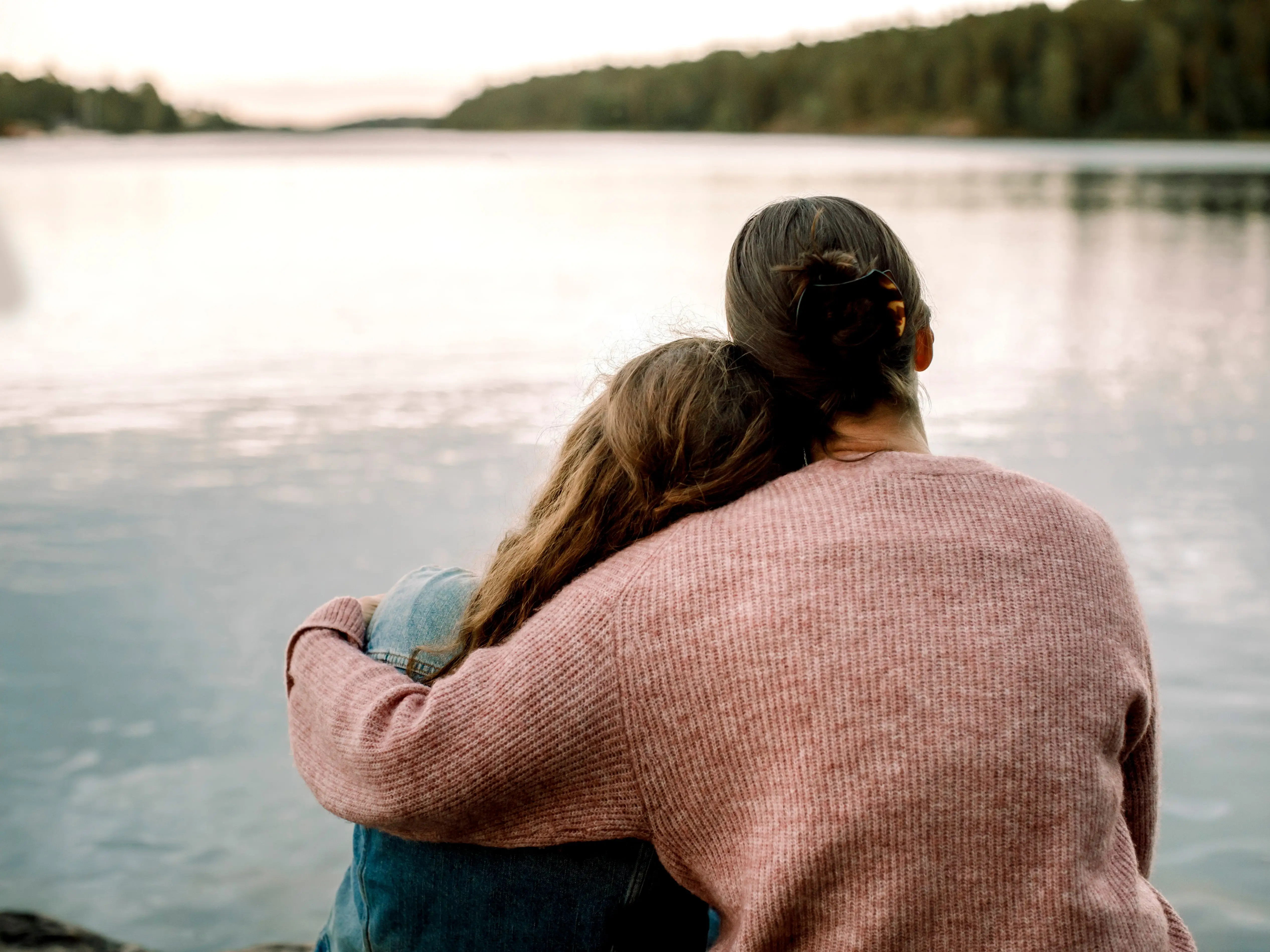 a woman and her daughter staring at a lake