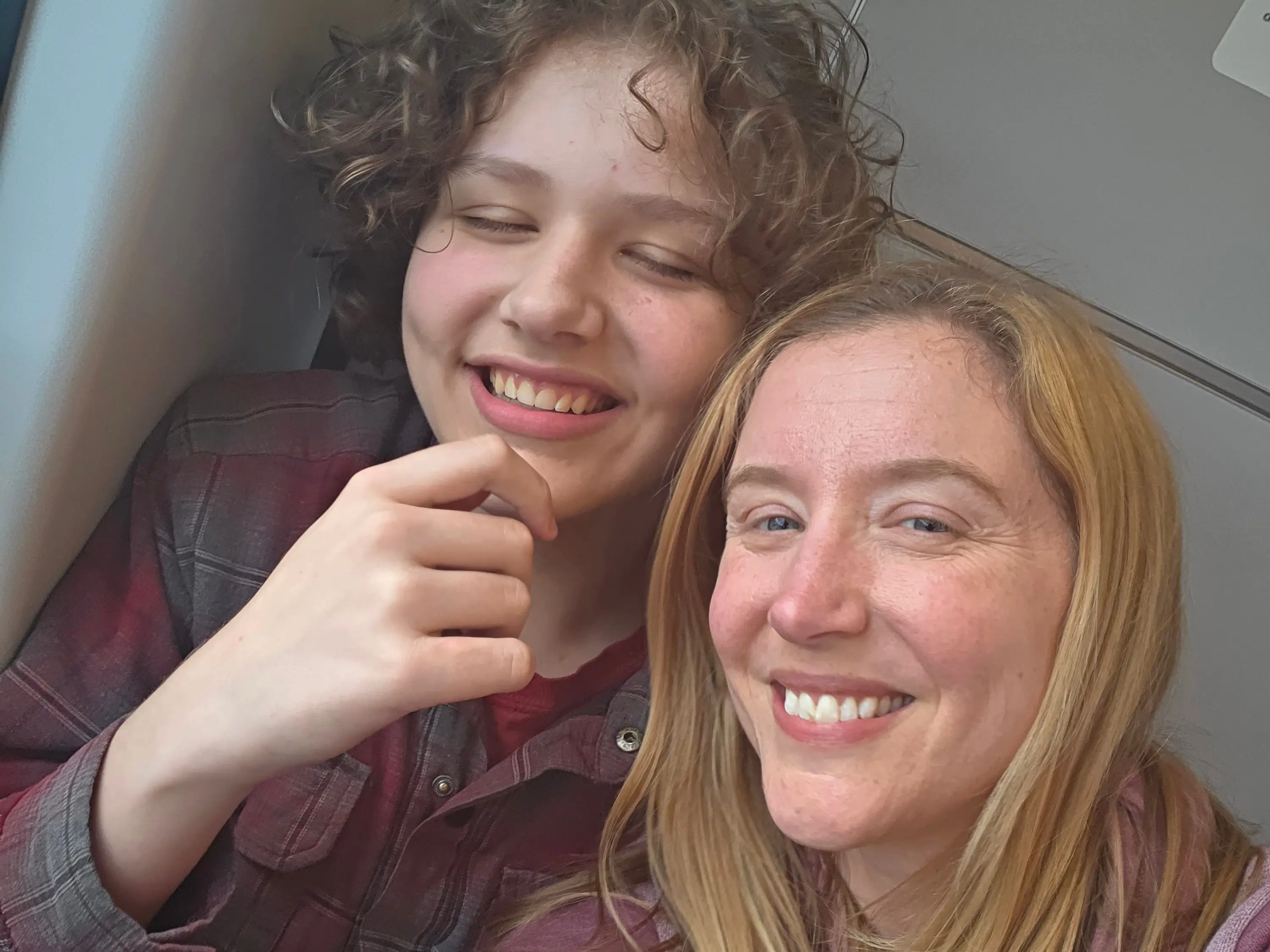 Two smiling people pose for a selfie beside a window in a passenger cabin.