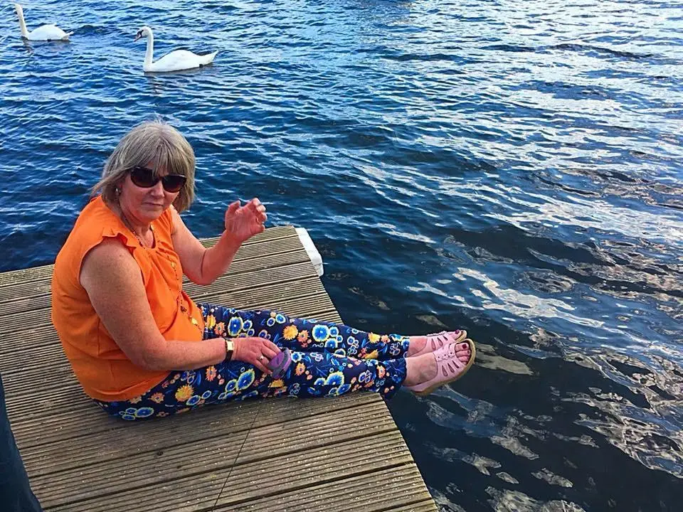 The author's mother sits on a dock with swans in the water nearby.