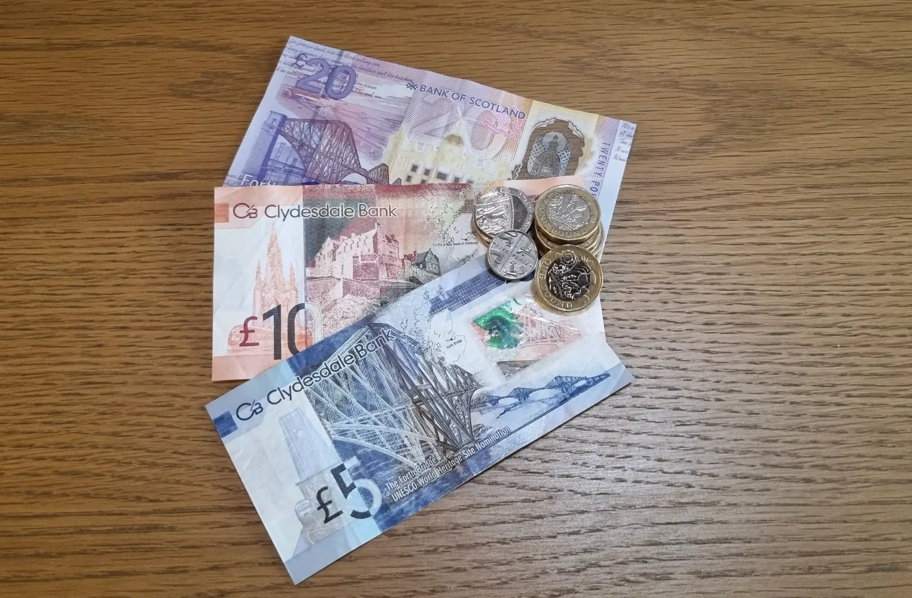A few Scottish banknotes and coins on a wood table.
