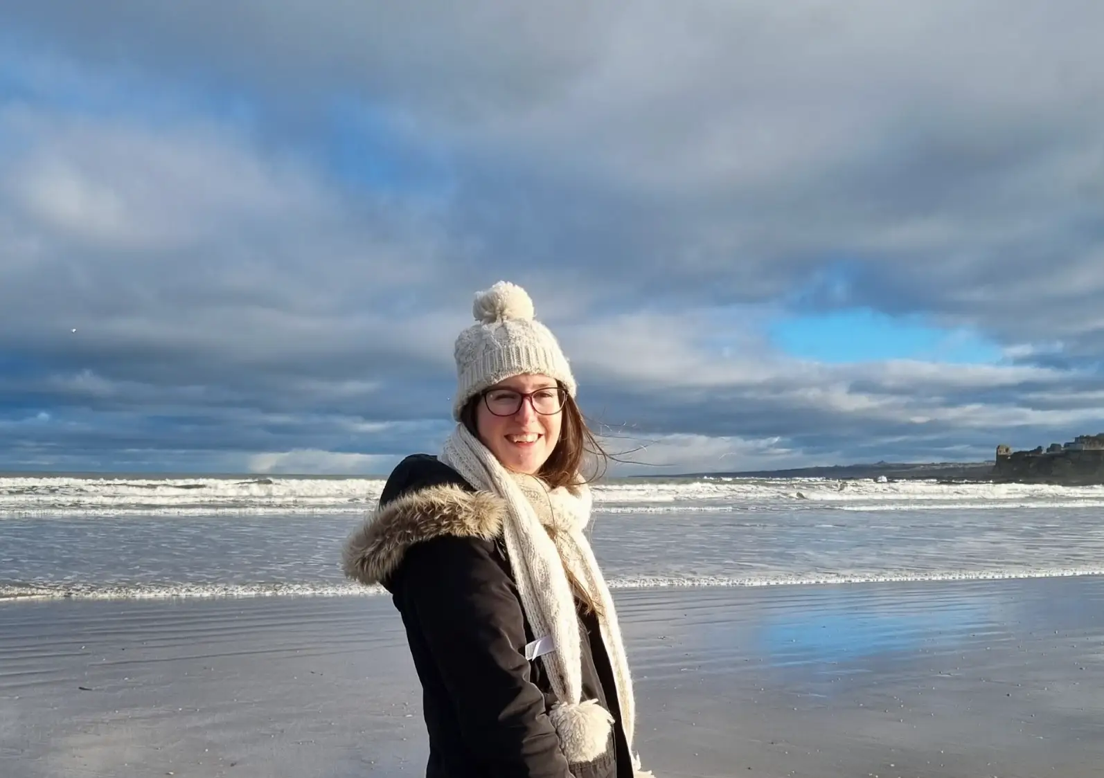 The writer standing on a beach, wearing a hat, coat, and scarf.