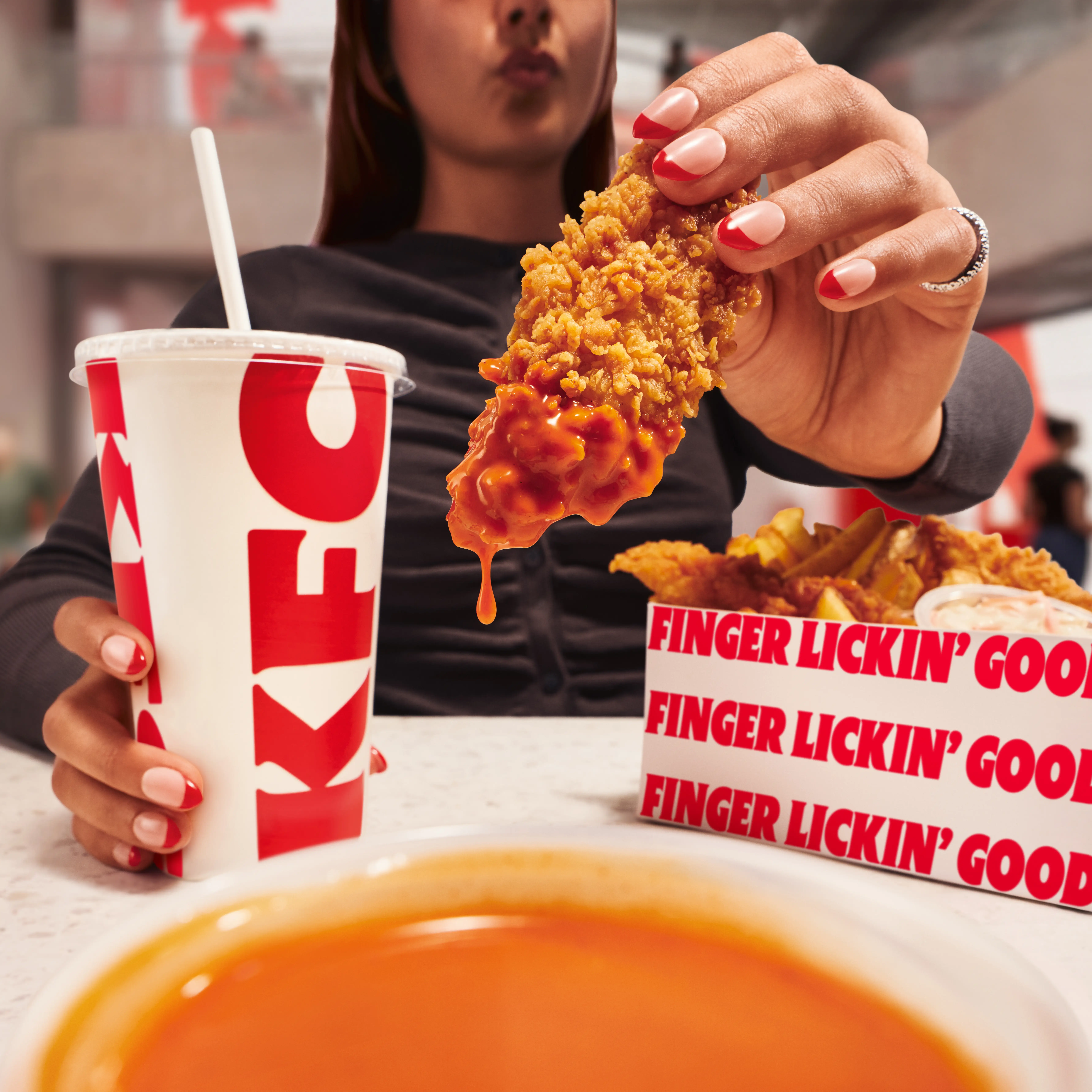 A KFC customer dips a chicken tender into a container of Buffalo sauce.