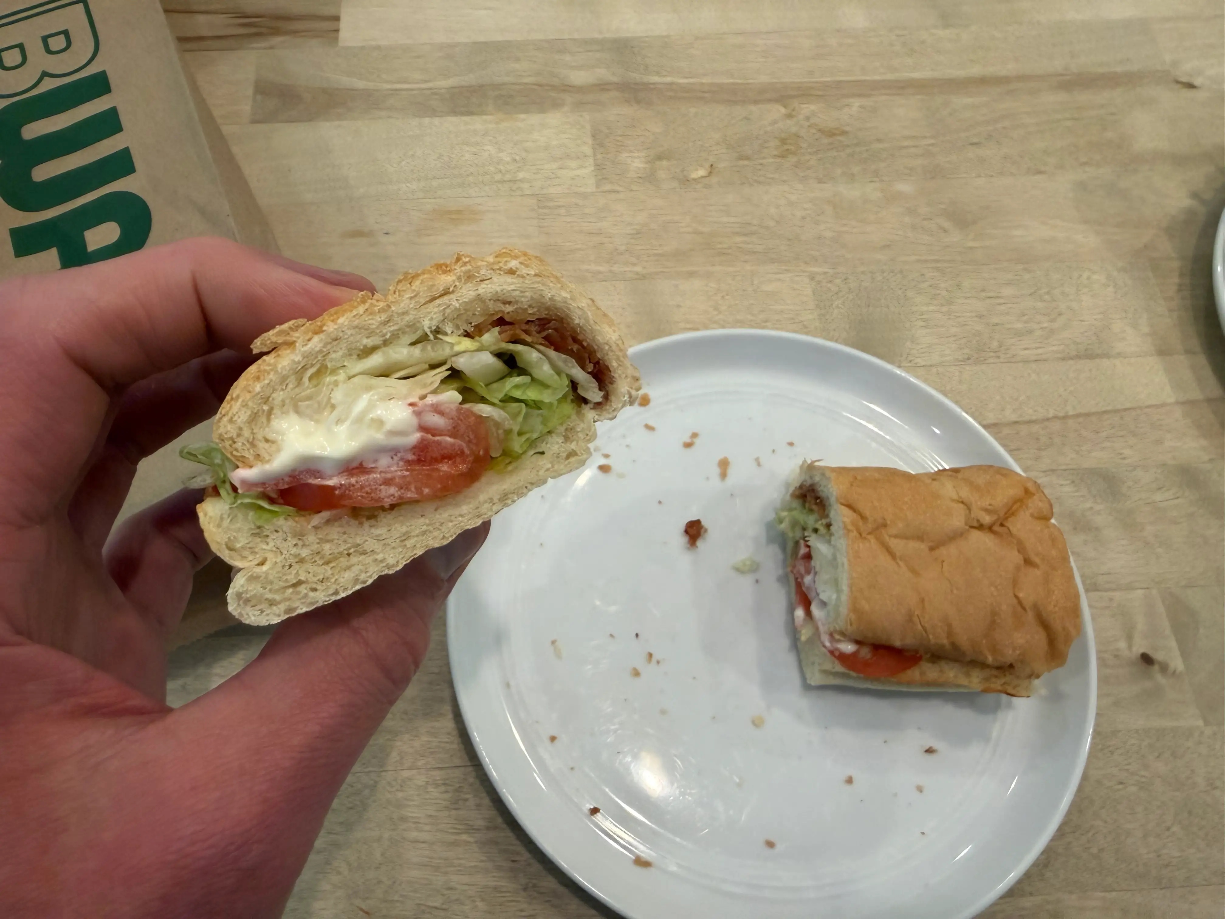 Hand holding sub sandwich half of BLT from Subway