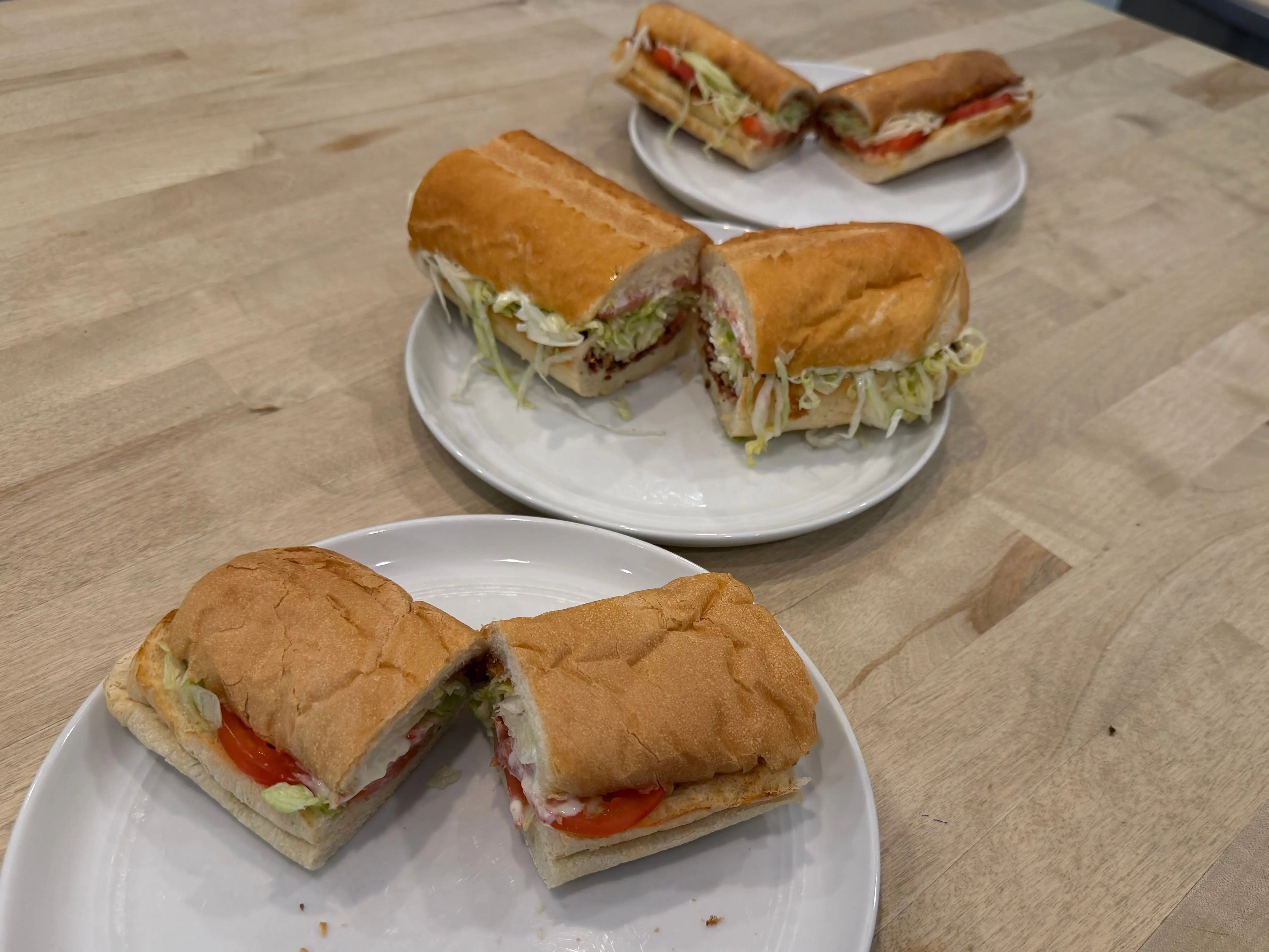 Three BLT sandwiches cut in half on plates on table