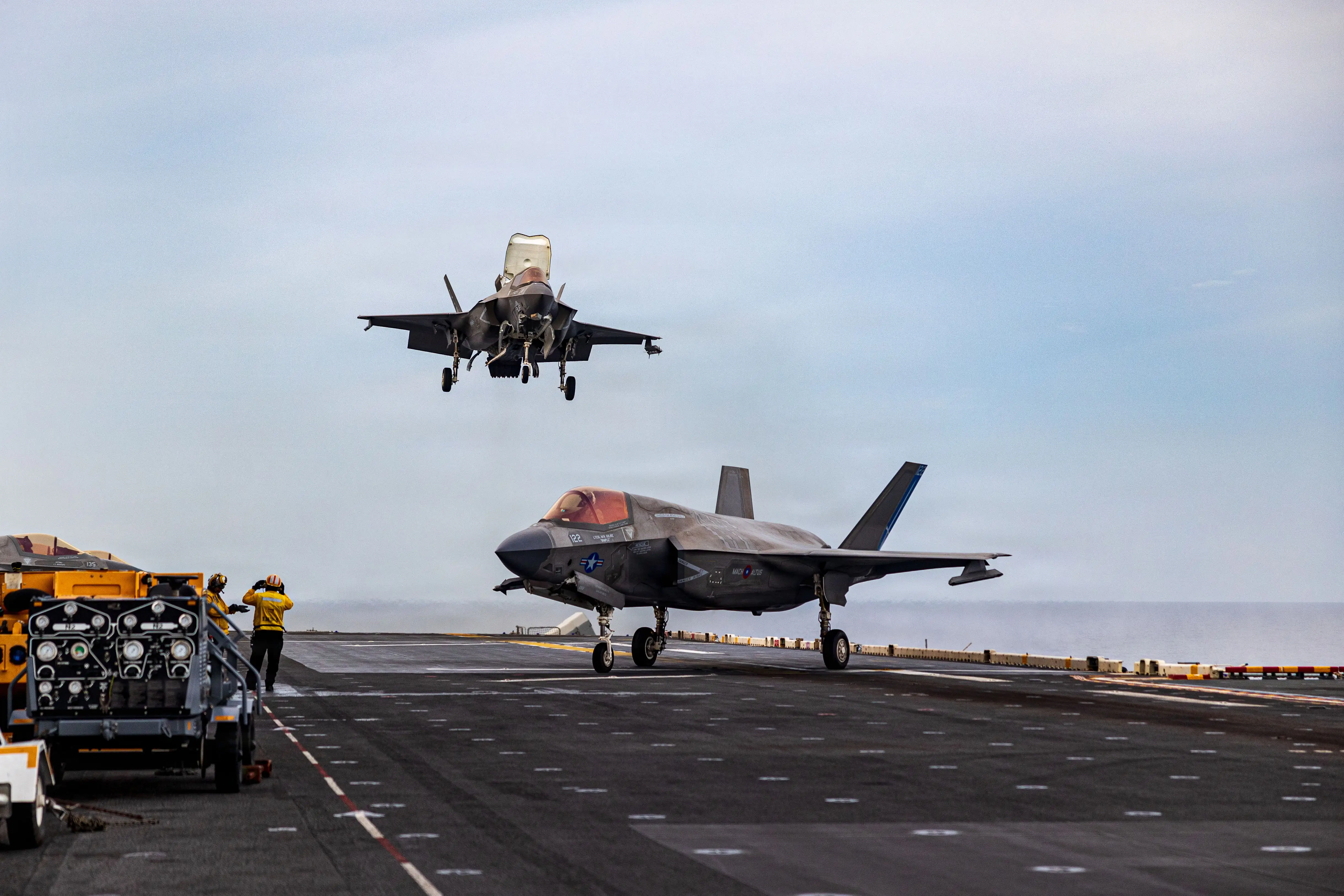 Two F-35s land on the deck of a vessel.