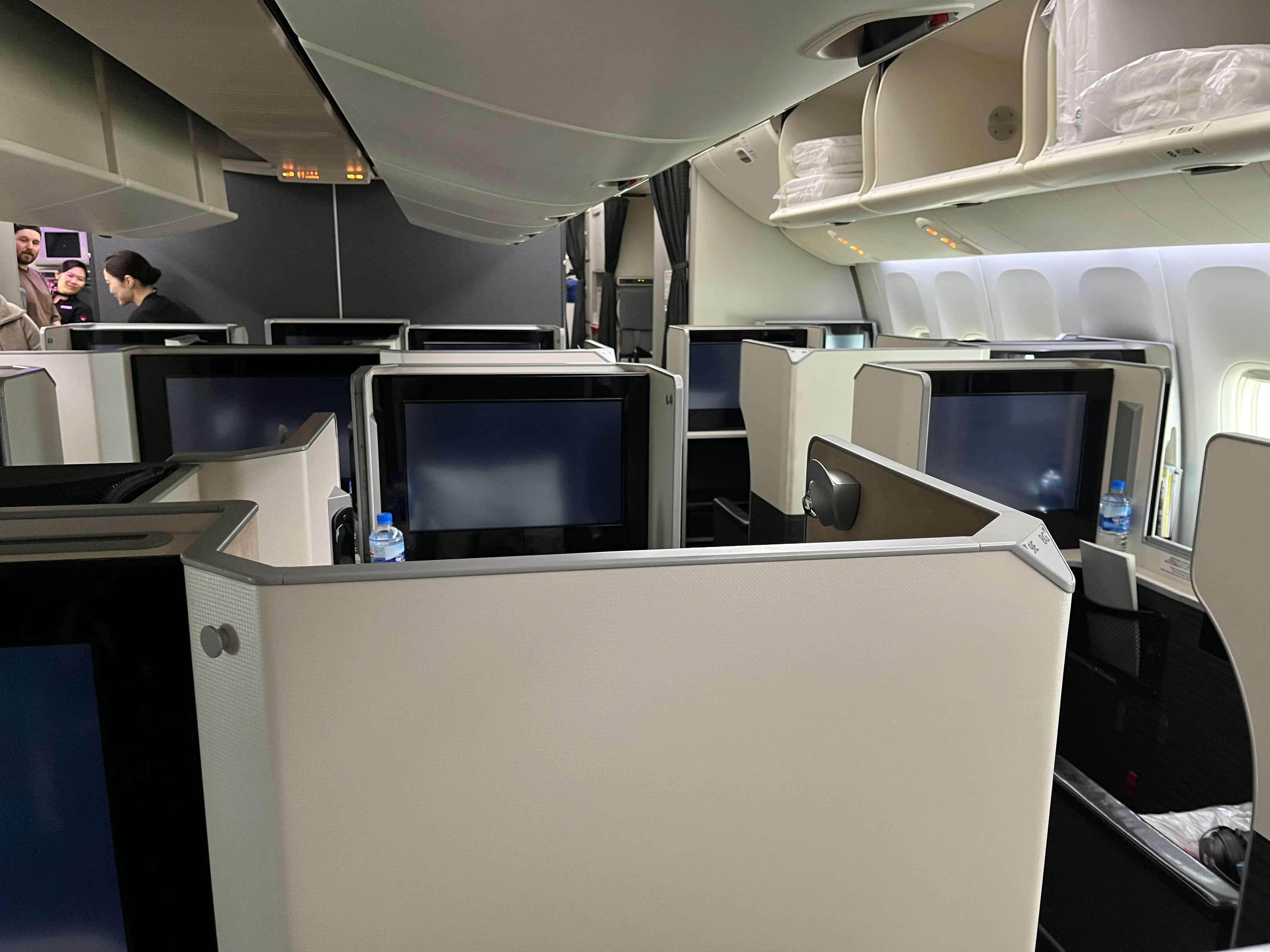 Business class airplane cabin with private suite seats, seatback screens, overhead bins, and window lighting on JAL