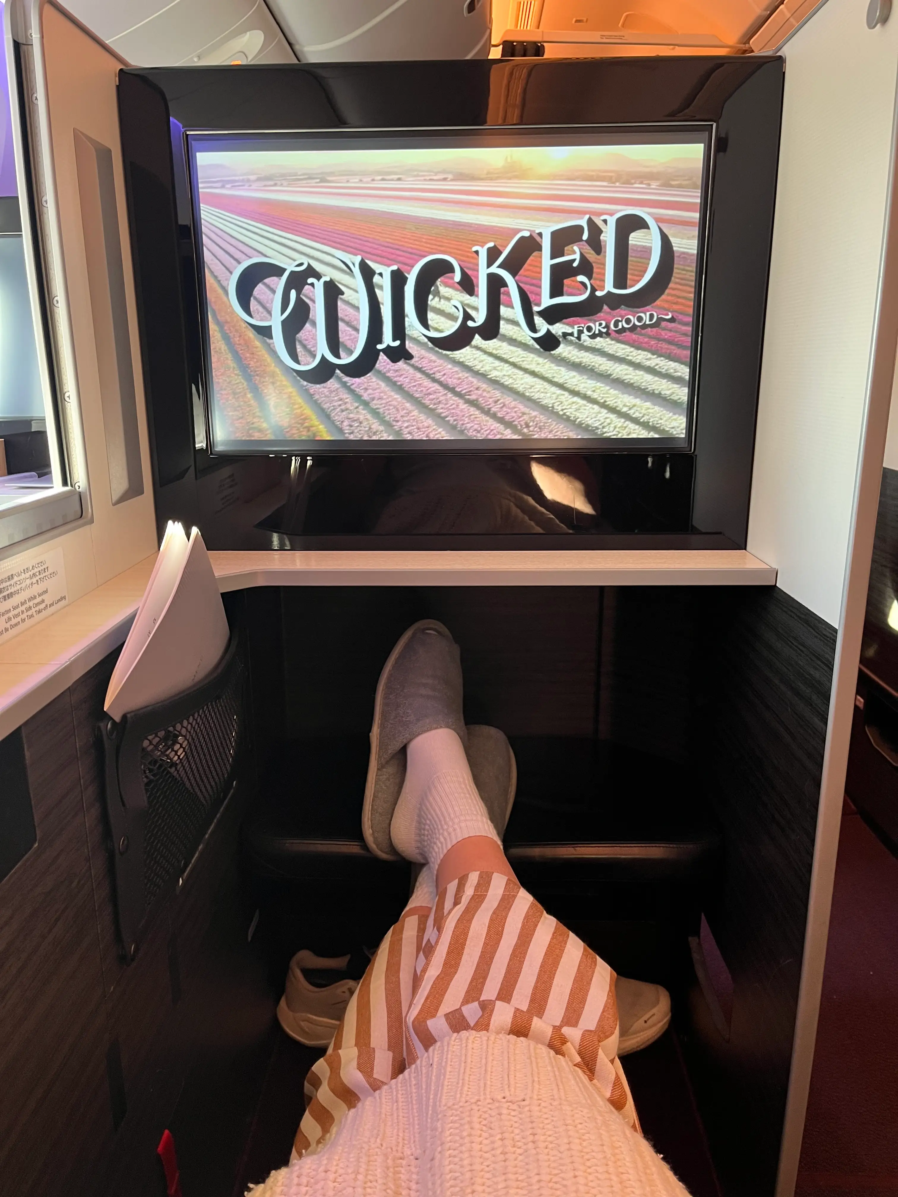 Wicked for good on seatback screen on plane with legs crossed below it