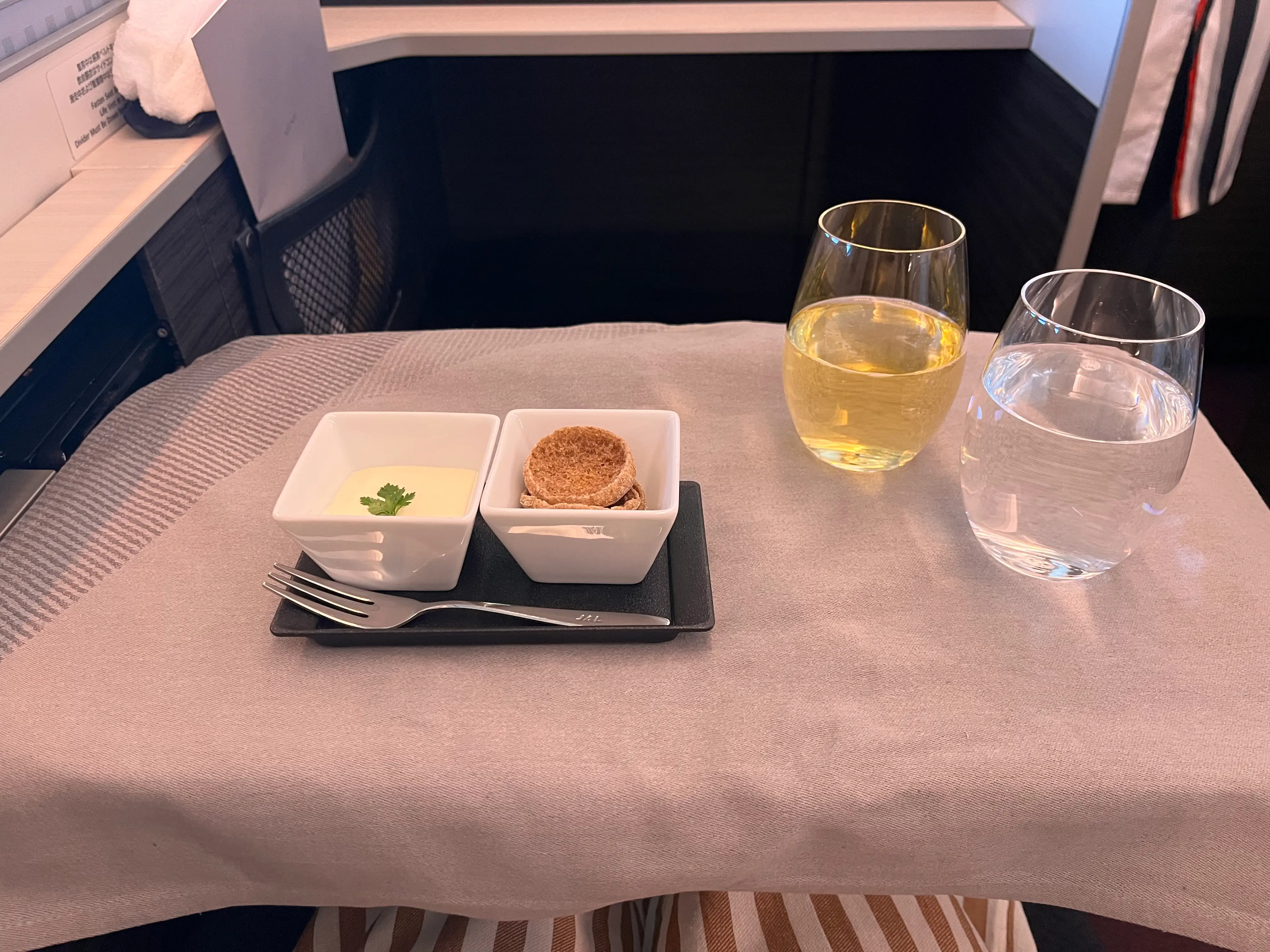 Gray tablecloth on plane tray table with food, two glasses of liquid