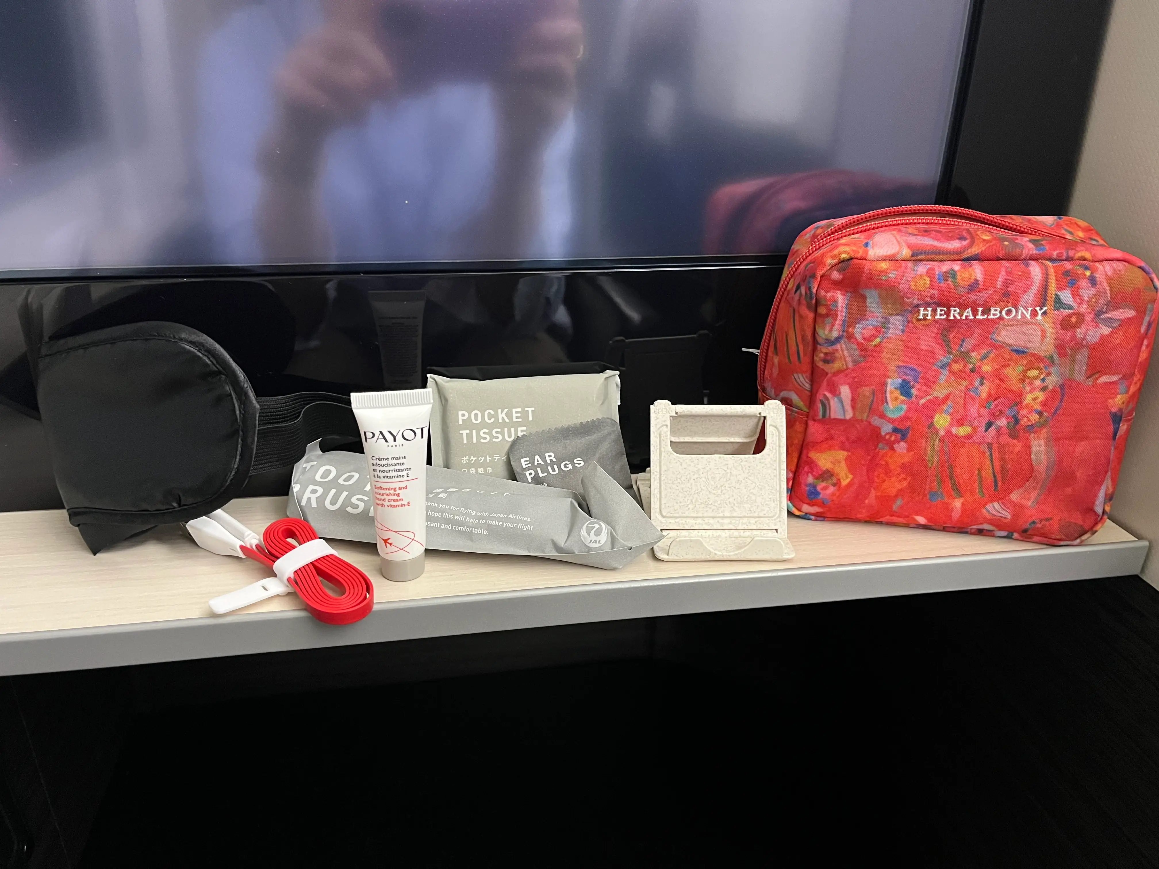 Heralbony amenity bag next to toothpaste, ear plugs, tissues, phone stand on shelf in business-class Japan Air seat