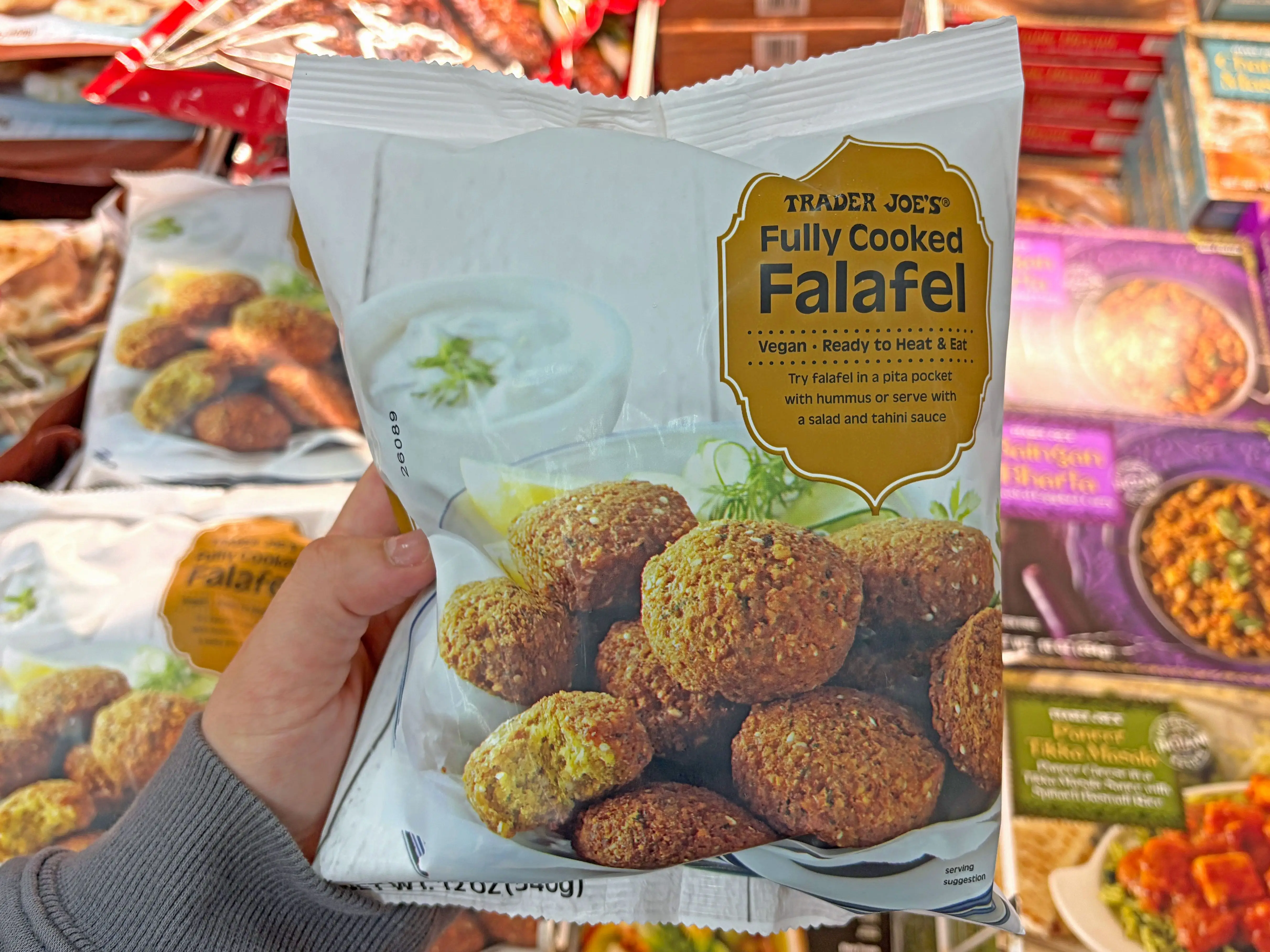 A hand holding a bag of Trader Joe's fully cooked falafel.