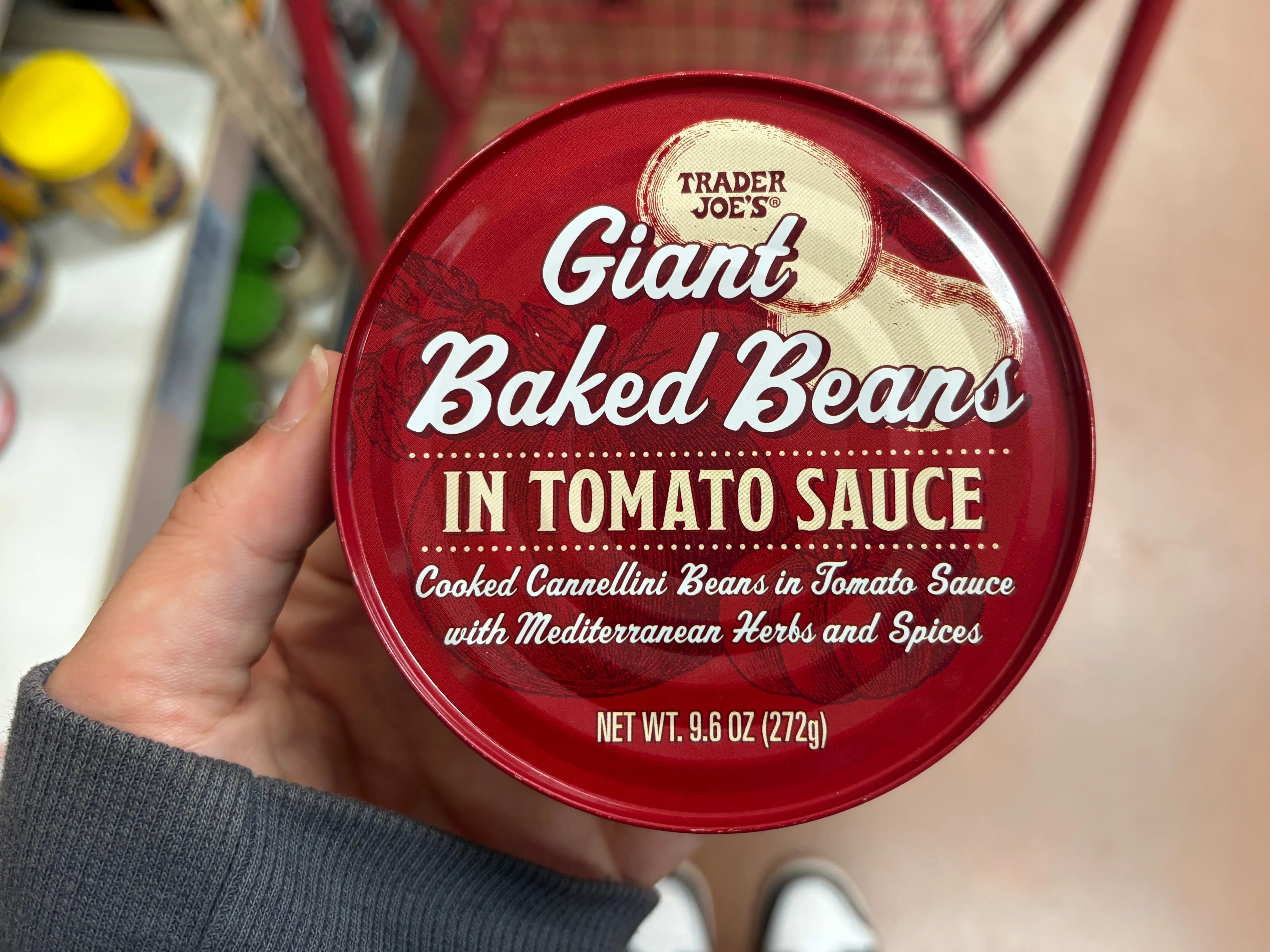A hand holding a container of Trader Joe's giant baked beans in tomato sauce.