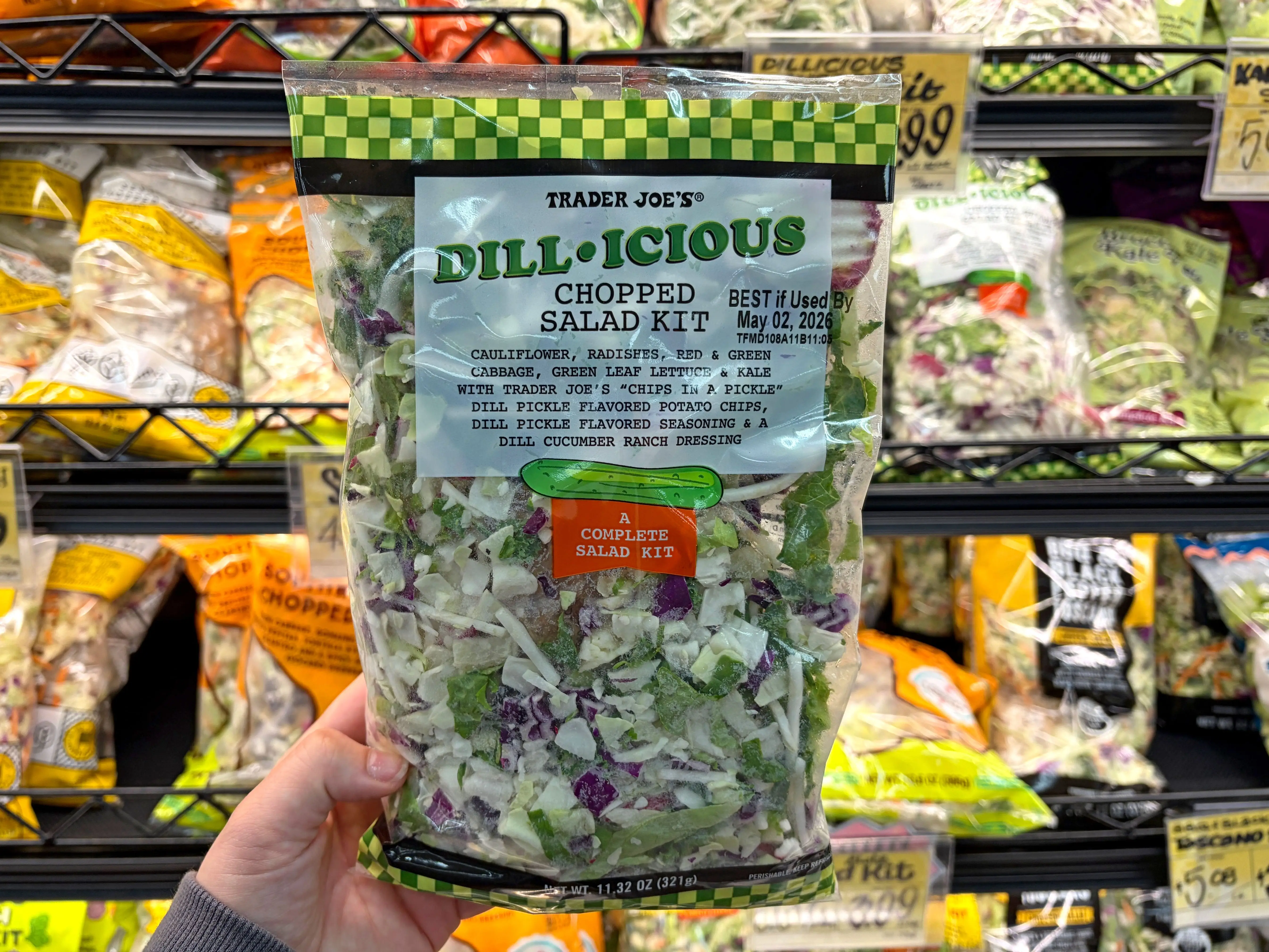 A hand holding a bag of Trader Joe's Dillicious chopped salad.