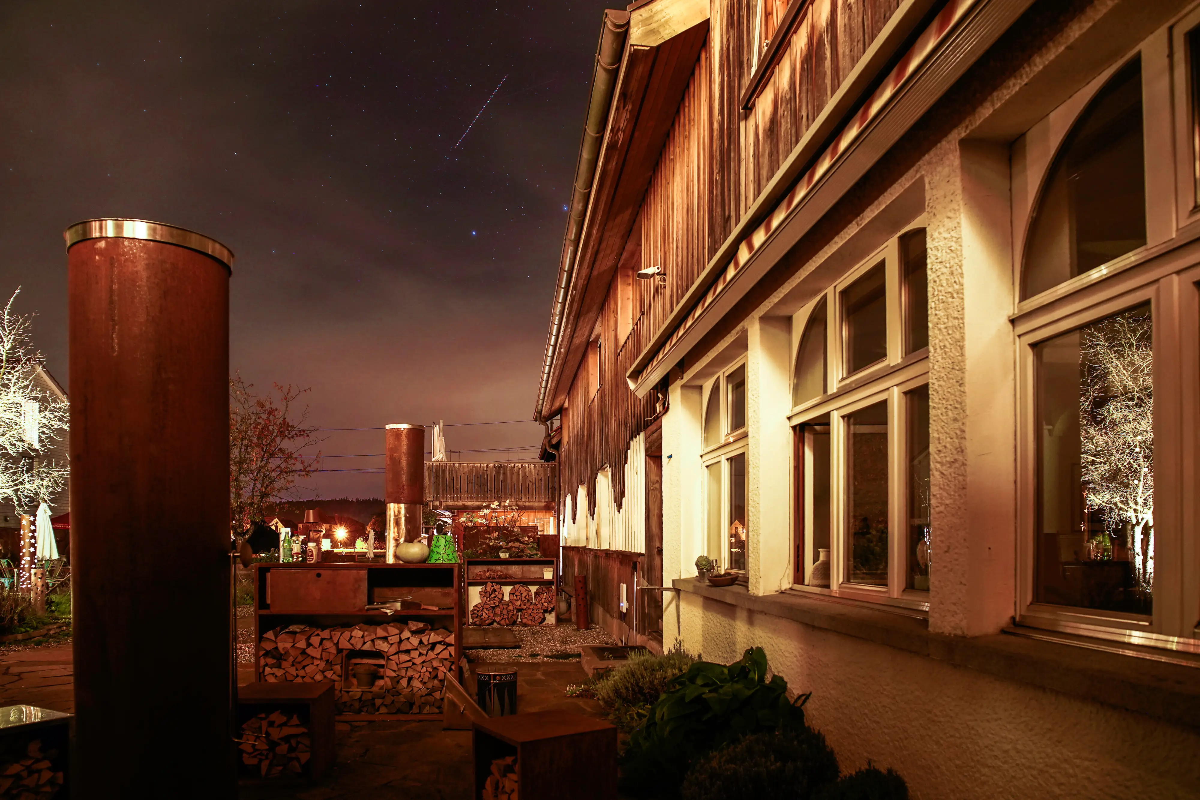 Fire pits and logs next to a house in Switzerland at night with stars in the sky